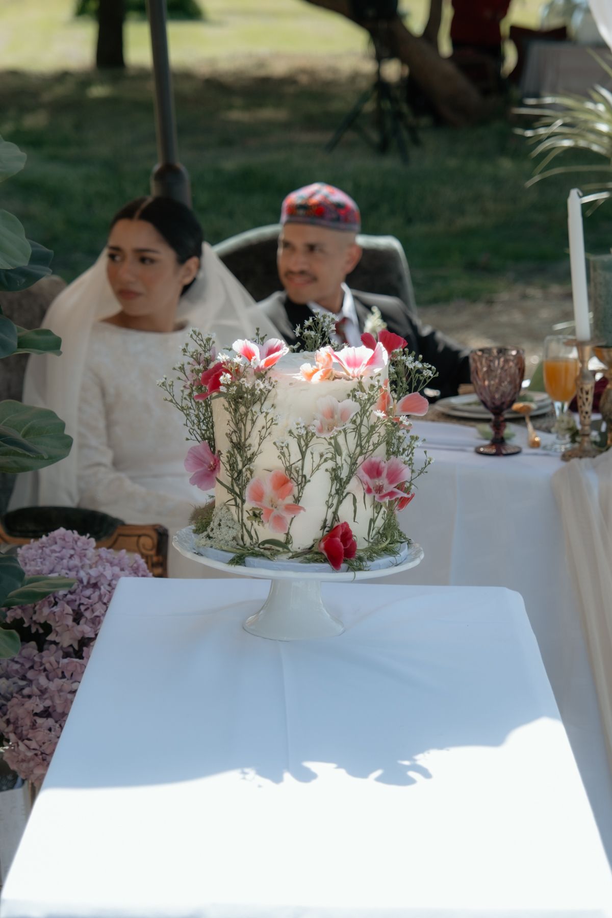 Elegant floral wedding cake with pink roses displayed at outdoor wedding reception table.