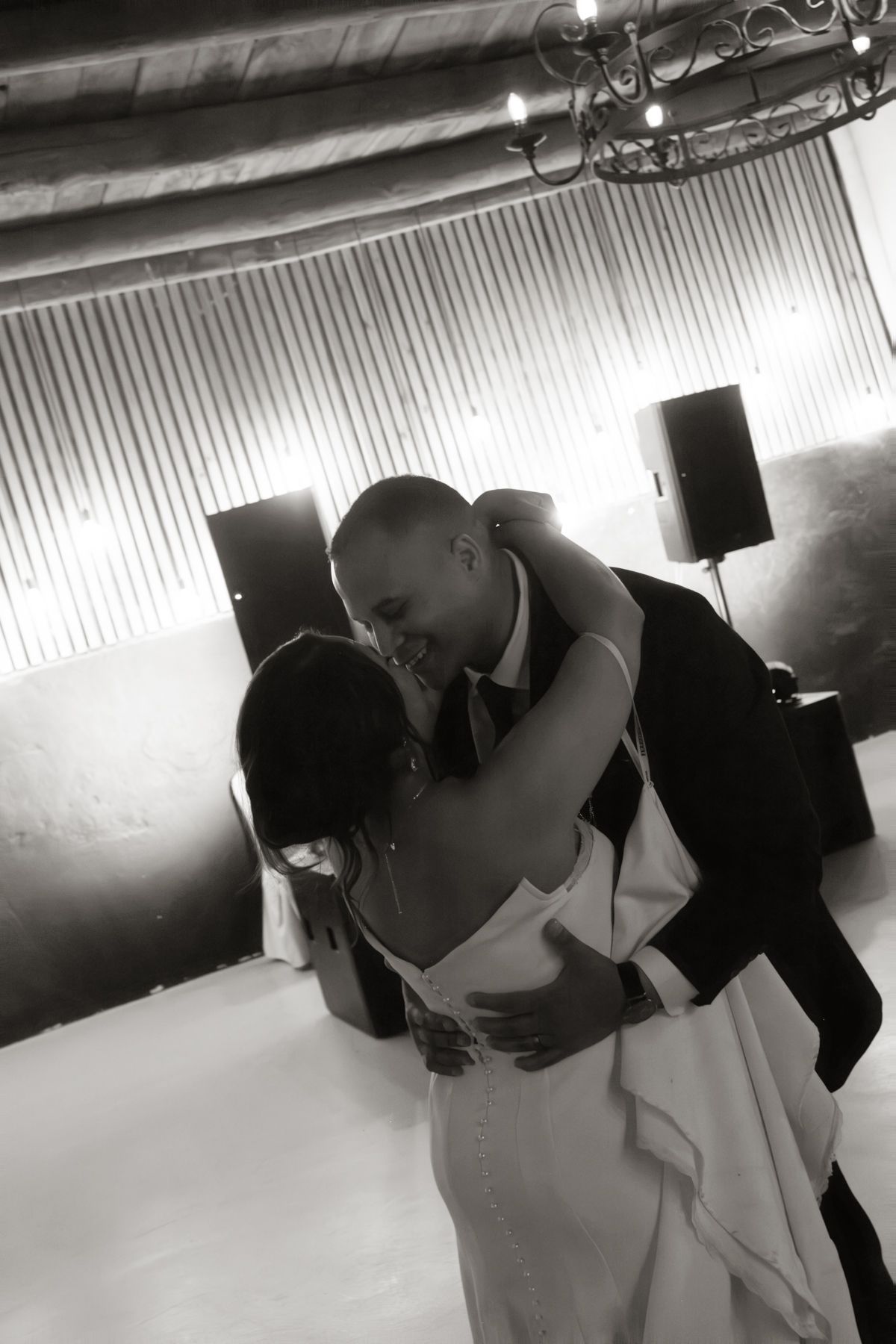 Black and white romantic first dance photo of bride and groom embracing on dance floor at wedding reception.