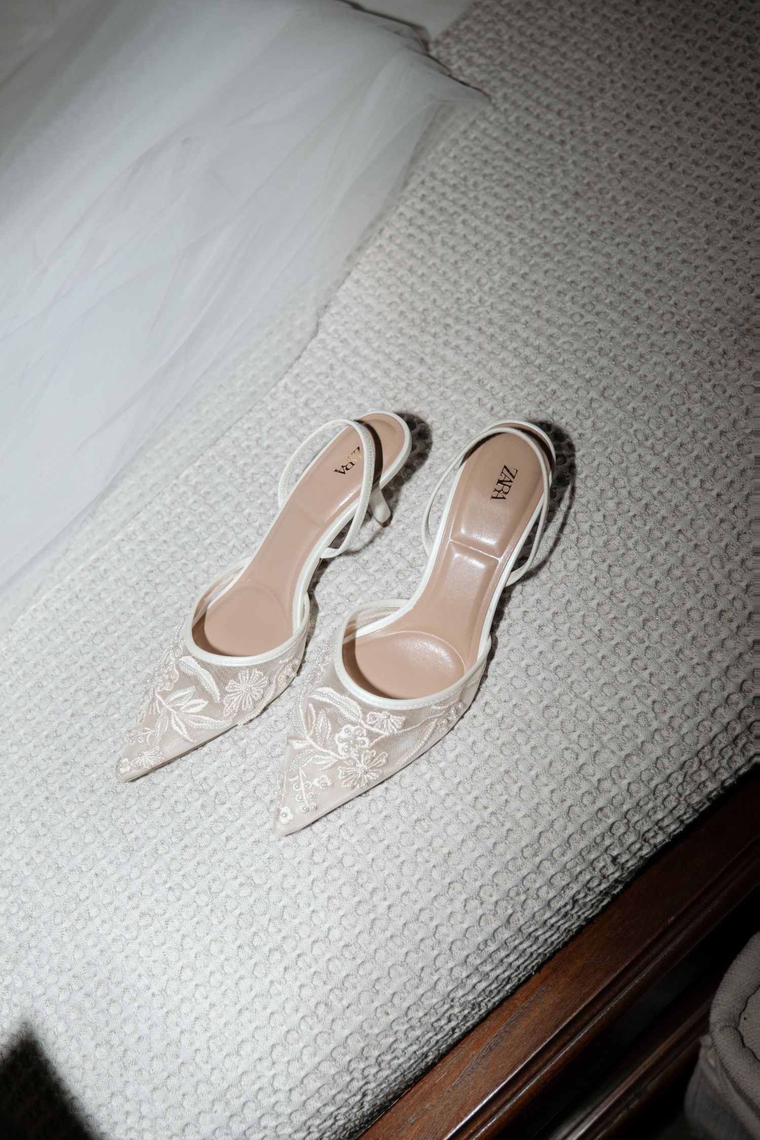 Elegant white lace Zara bridal heels with pointed toe and slingback strap displayed on a white textured bedspread.