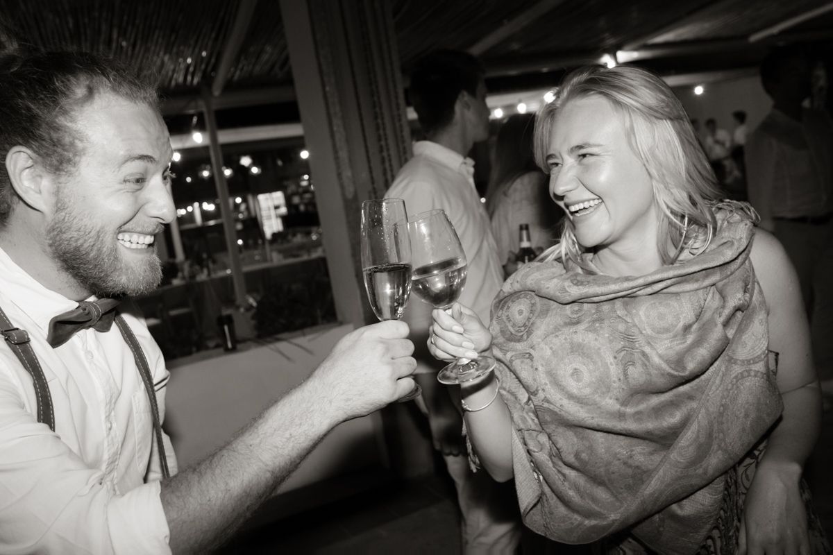 Man in bow tie and woman laughing while toasting with champagne glasses at a wedding reception.