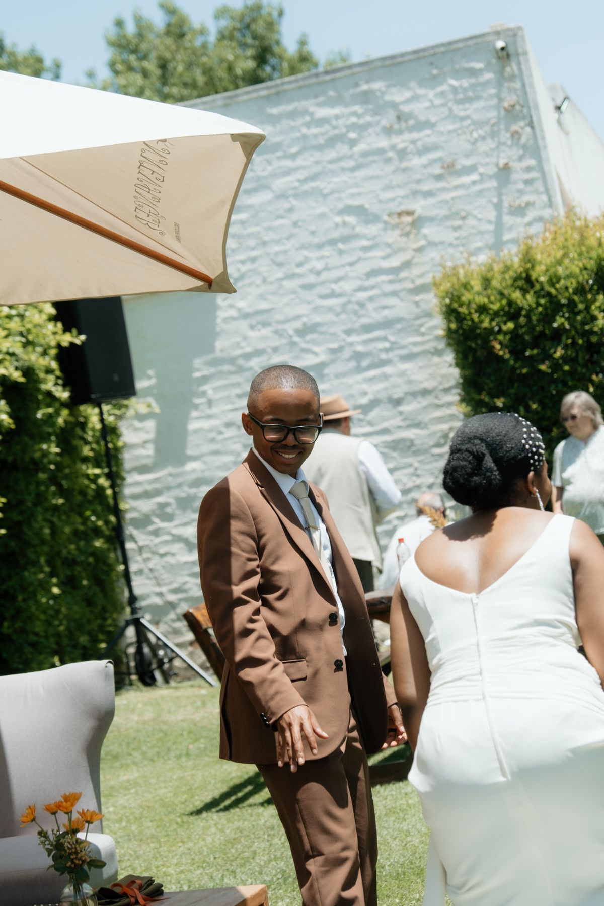 Young boy in brown suit greets bride in white dress at sunny outdoor wedding celebration.