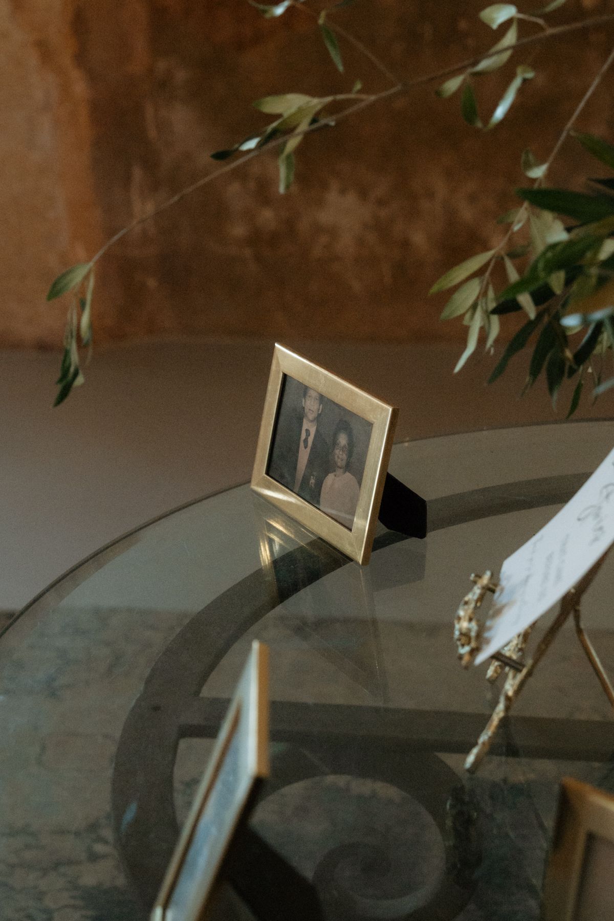 Small framed wedding photo of couple displayed on glass table with olive branch decoration.