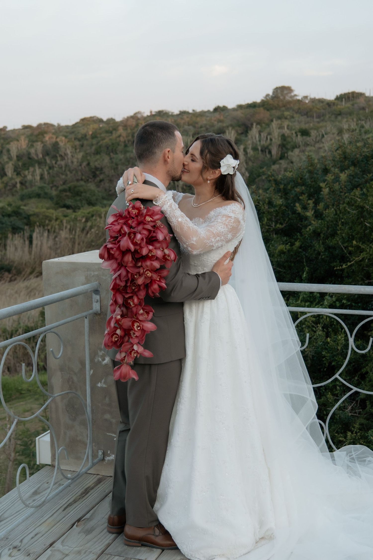 Bride and groom sharing a kiss on balcony with lush green landscape in background.