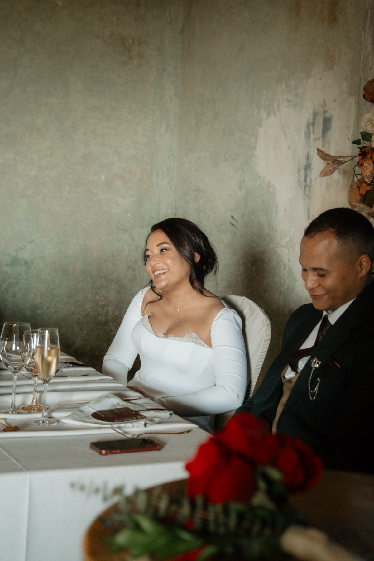 Bride laughing joyfully at the wedding reception dinner table decorated with red roses and champagne glasses.