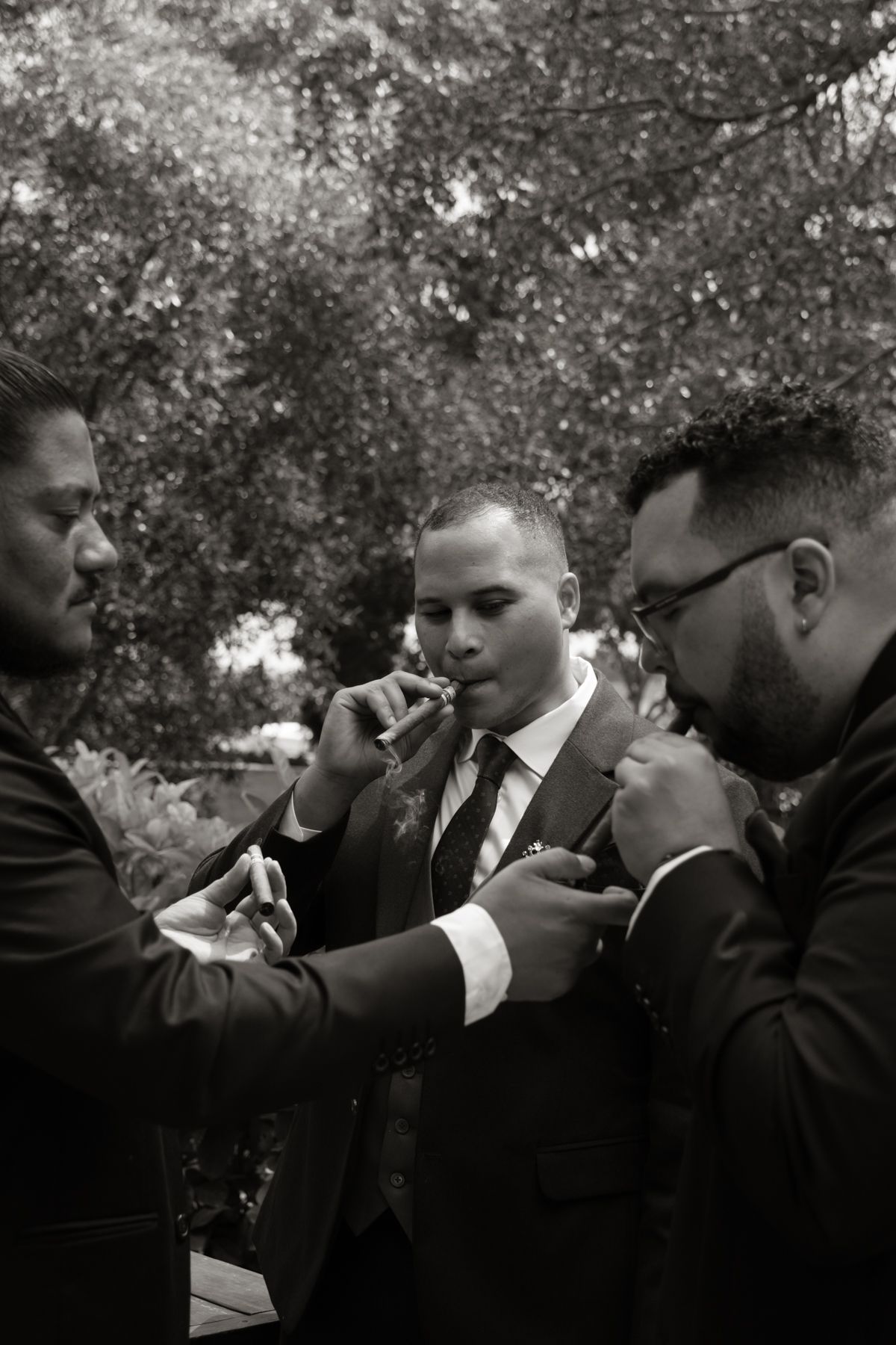 Black and white photo of groomsmen helping groom with boutonniere before outdoor wedding ceremony.