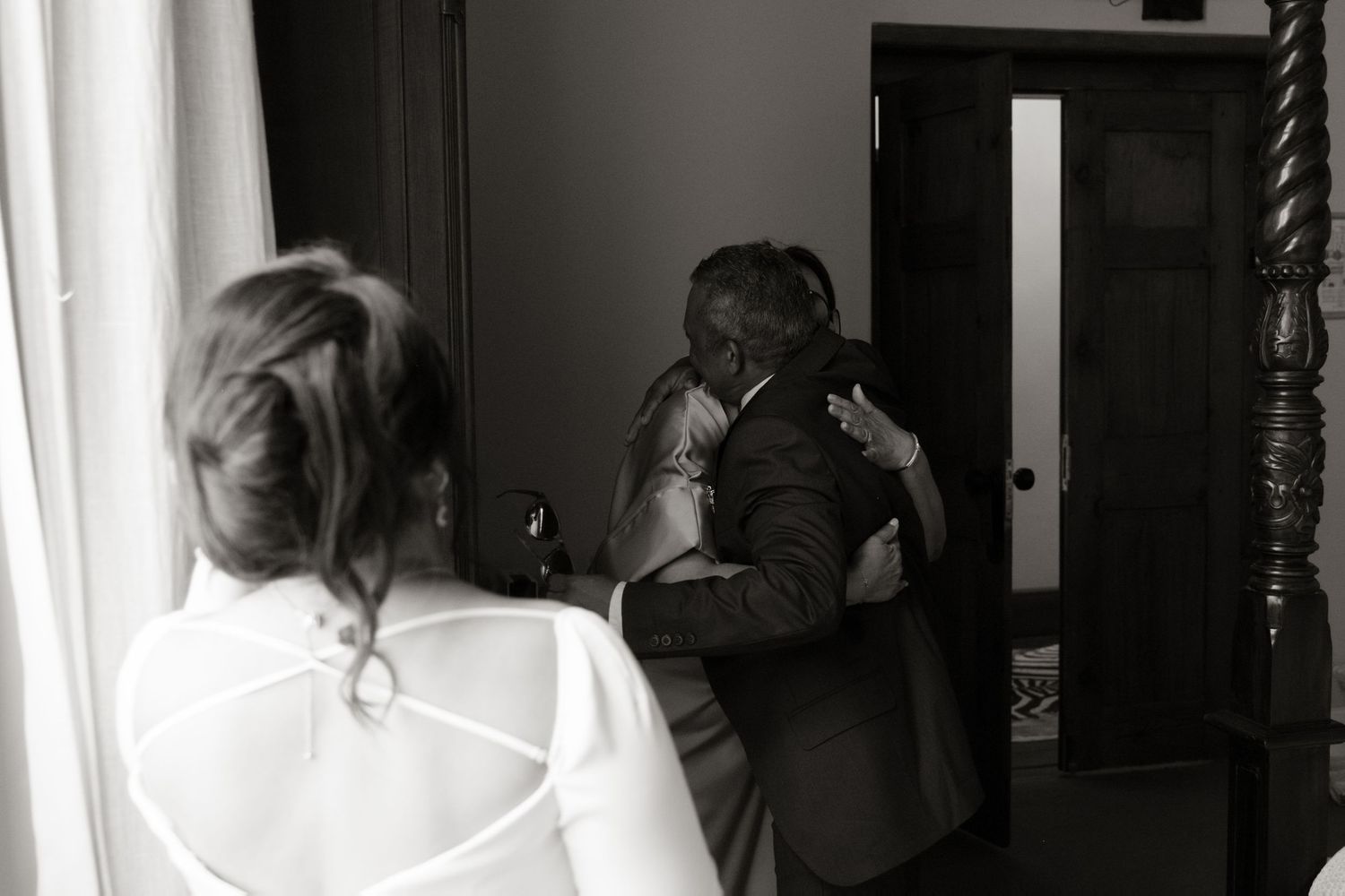 Black and white wedding photo of bride watching couple embrace in doorway.