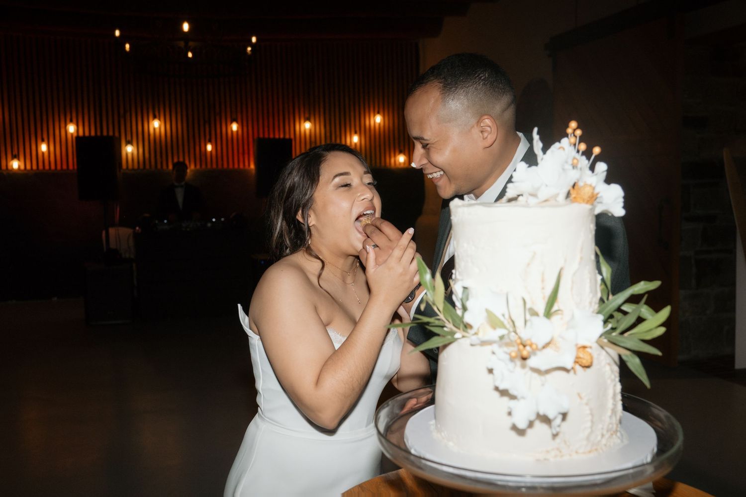 Smiling bride and groom share a joyful cake cutting moment at their wedding reception.