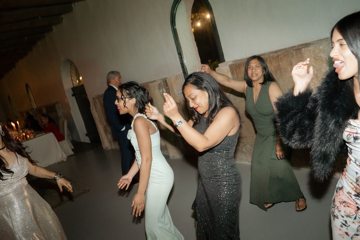 Guests in formal attire dance energetically together on the wedding reception dance floor at night.