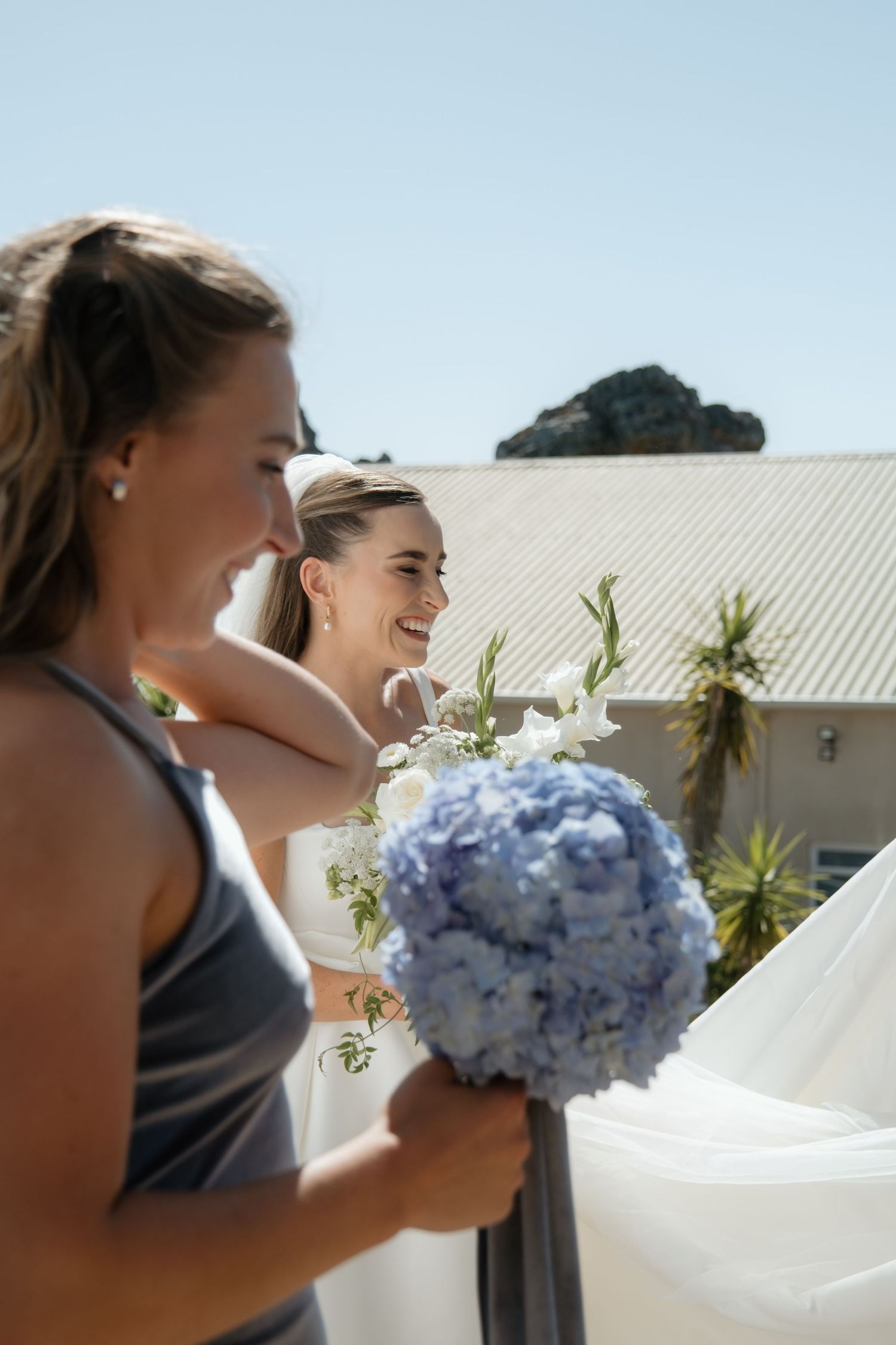 Two people in formal attire share a joyful moment outdoors while holding a blue hydrangea bouquet.