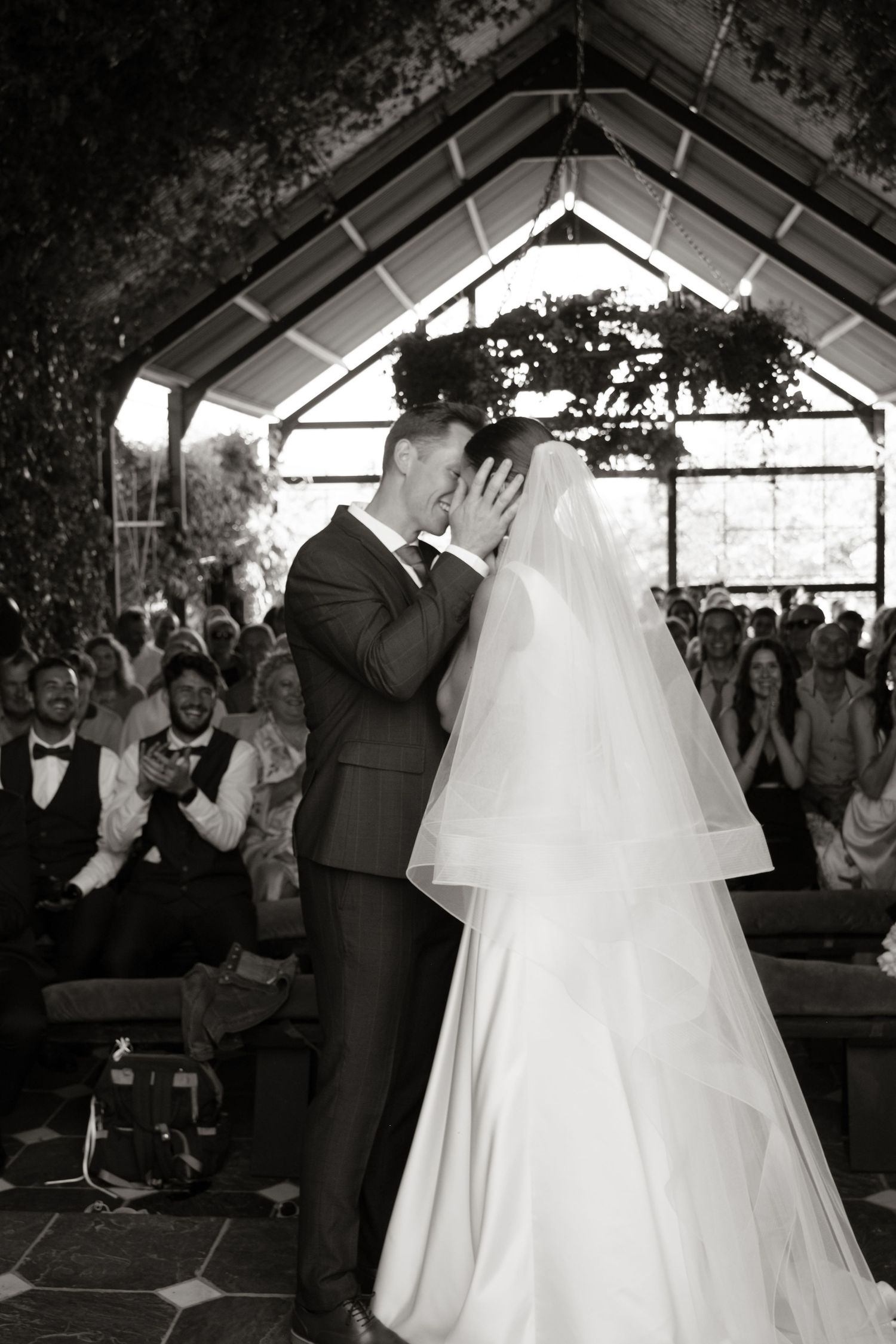 Bride and groom share their first kiss at the altar in a black and white wedding ceremony photo.