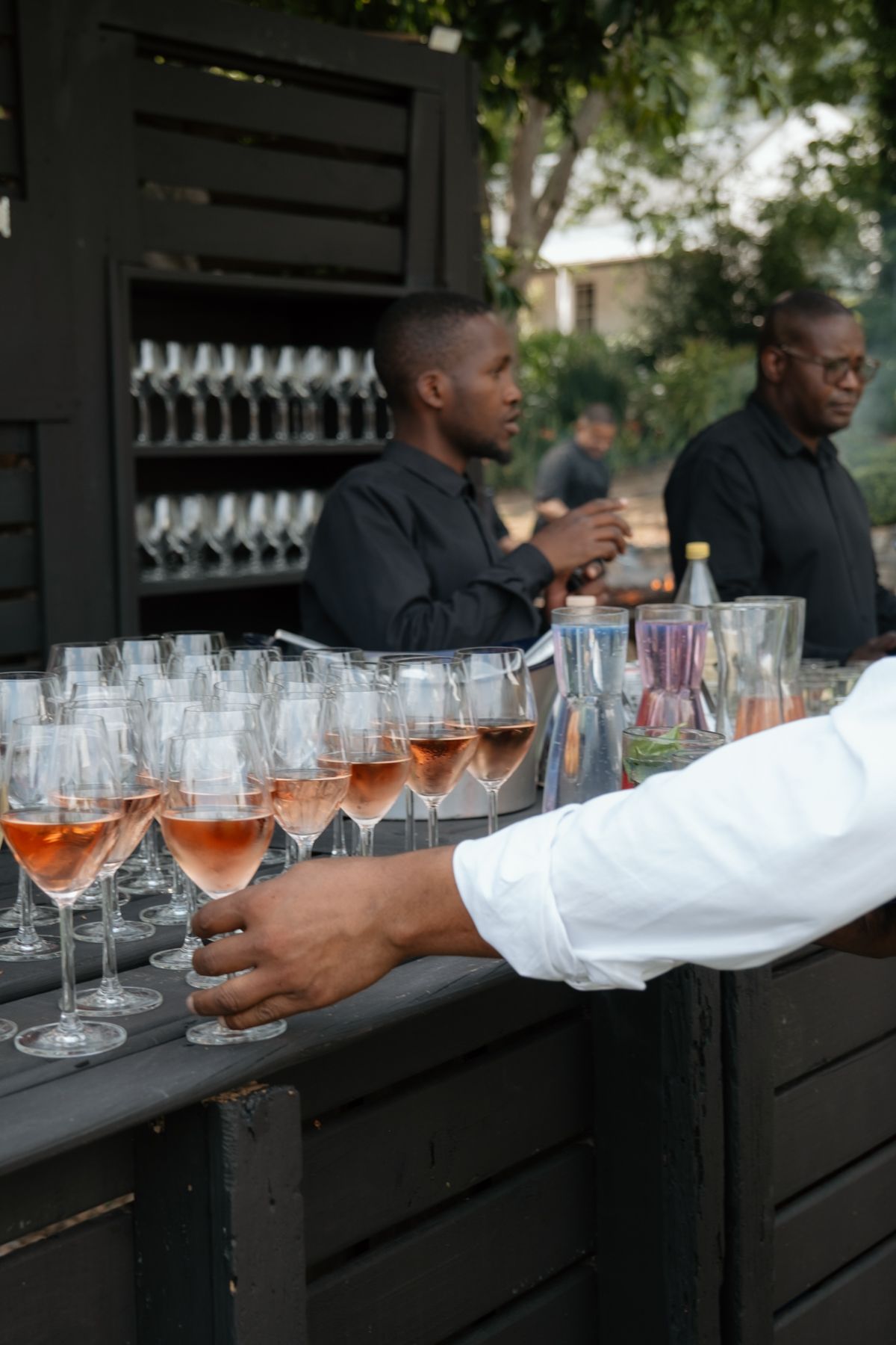 Wedding reception bar service with rose wine glasses arranged on dark wooden counter.