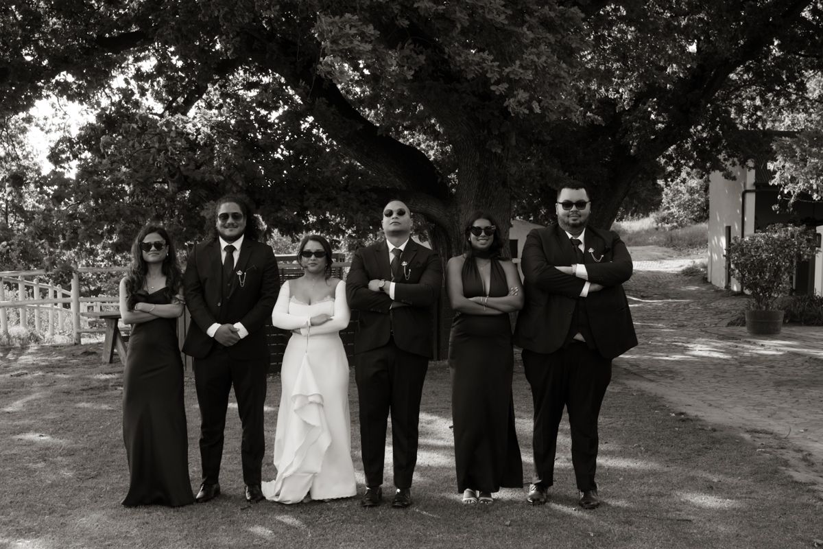 Black and white photo of a wedding party of six posing under a tree with arms crossed in a stylish pose.
