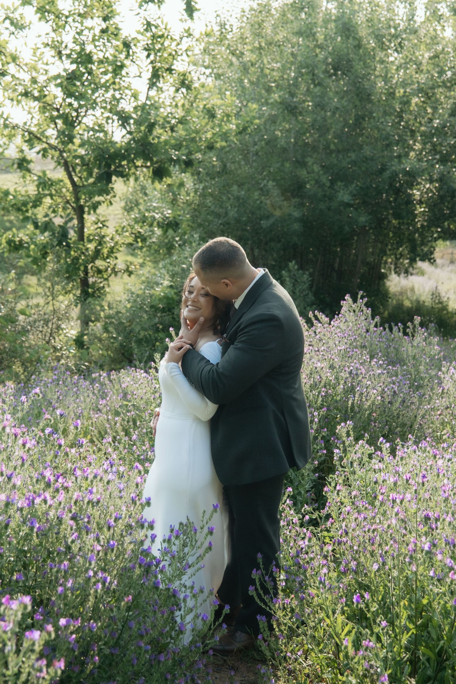 Bride and groom embrace tenderly in a field of purple wildflowers during golden hour wedding photos.