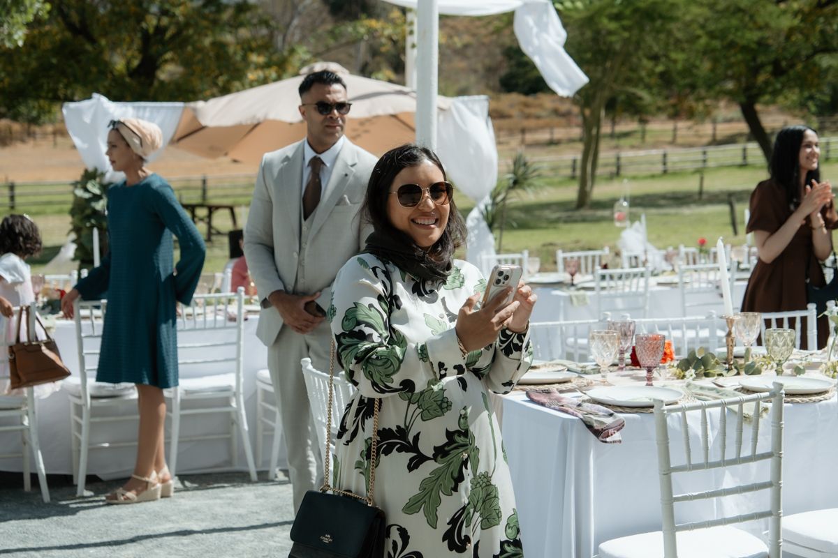 Wedding guest taking a selfie at an outdoor reception with white draped tables in background.