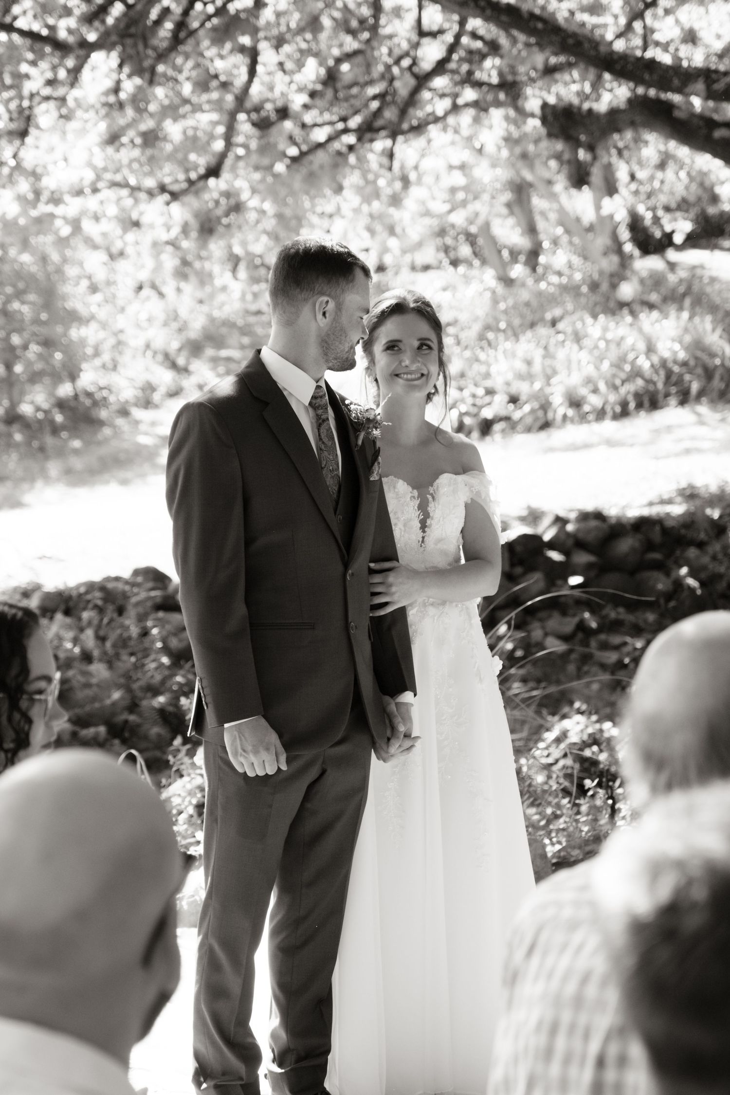 Black and white photo of bride and groom sharing a tender moment during outdoor wedding ceremony.