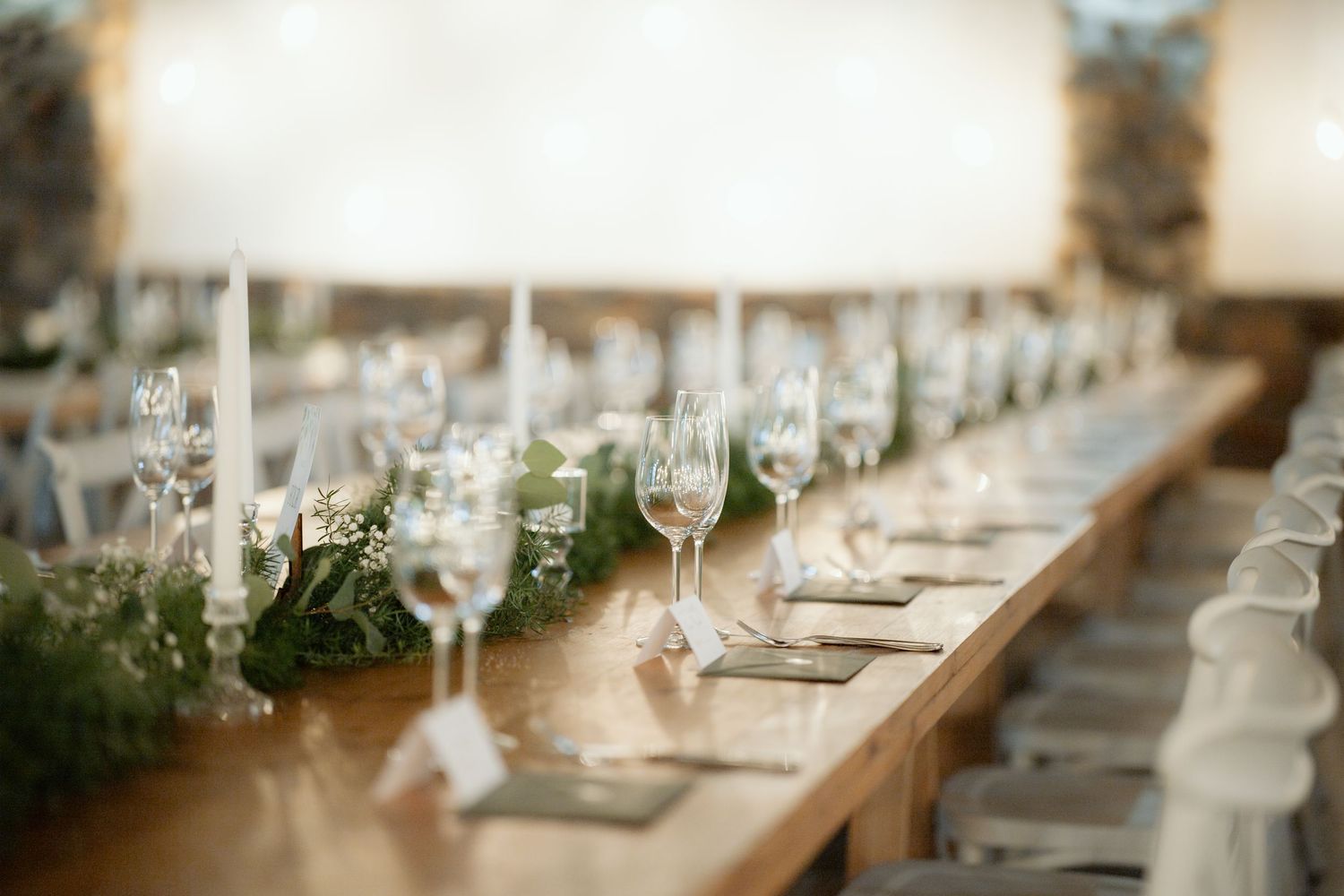Elegant wedding reception table with candles, crystal glasses, and greenery garland on a rustic wooden farm table.