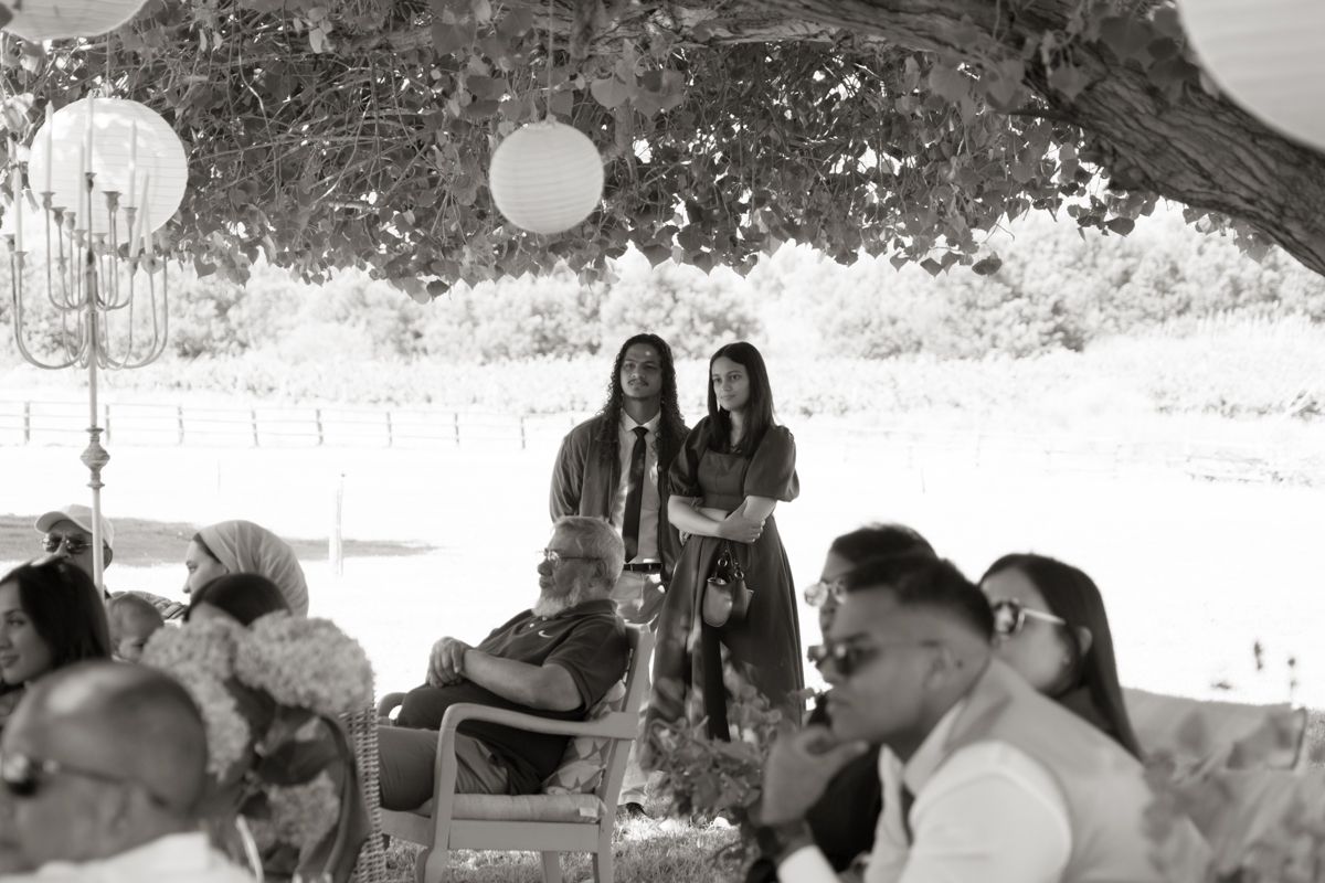 Black and white photo of two women speaking at outdoor wedding ceremony under decorated tree.