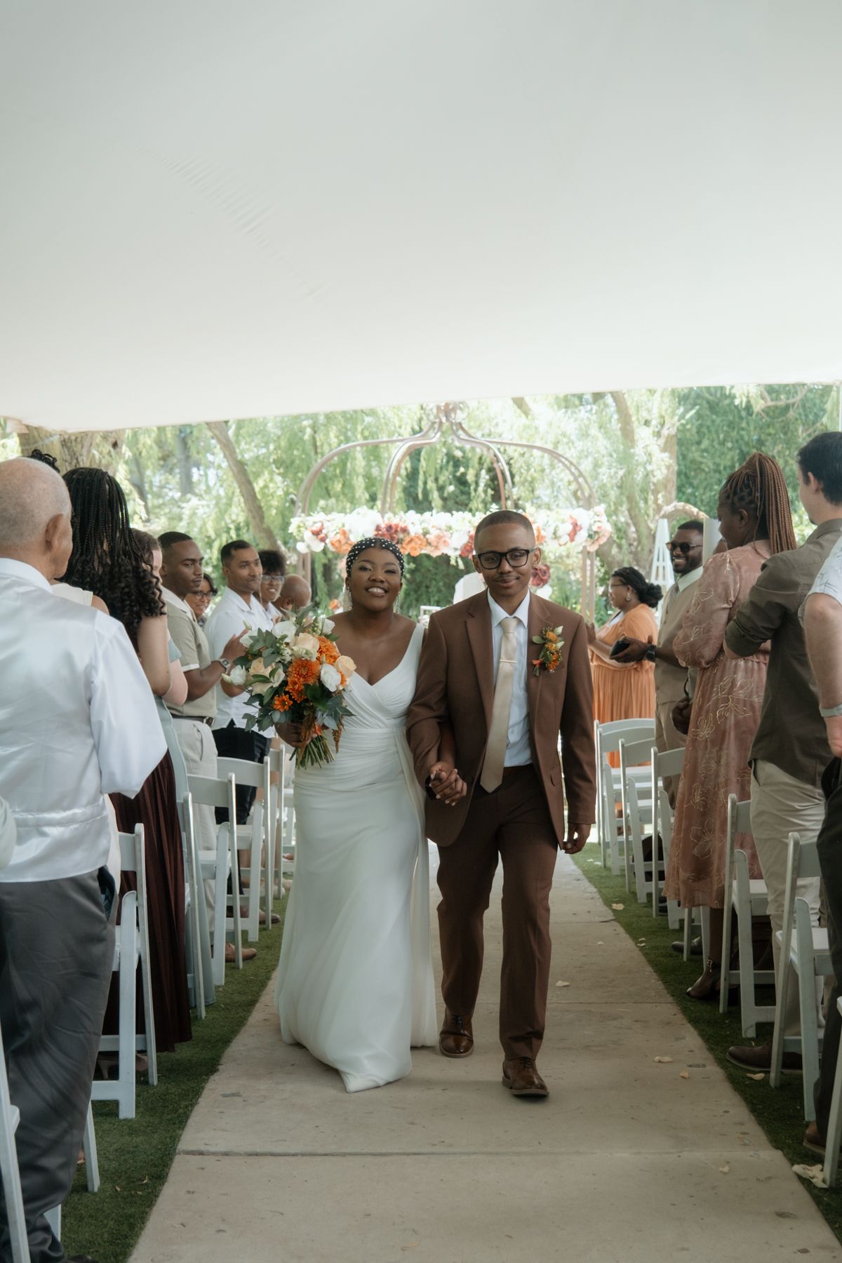 Joyful newlywed couple walks down the aisle hand-in-hand after their outdoor wedding ceremony.