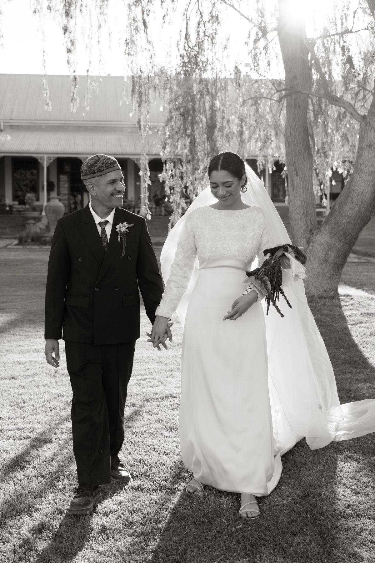 Black and white photo of happy bride and groom walking hand in hand on a sunny wedding day.