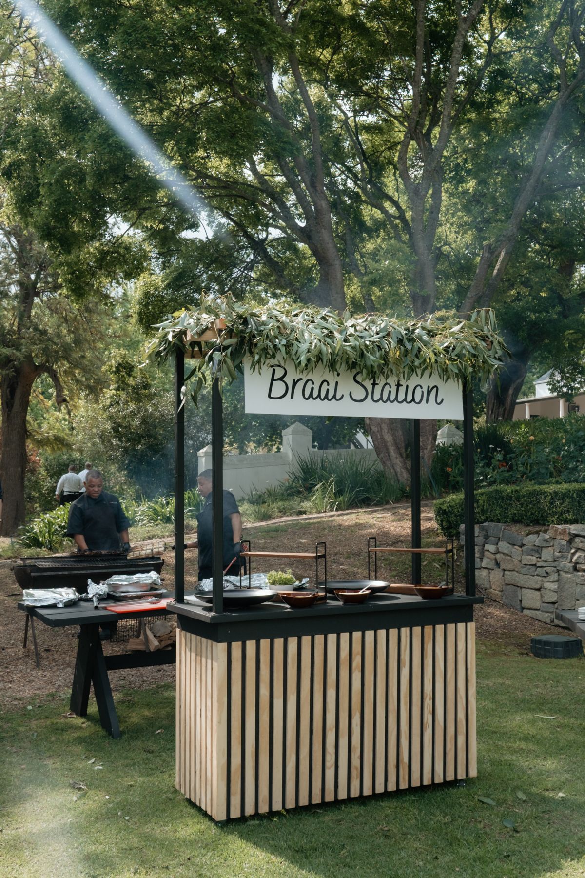 Outdoor braai station food stall decorated with greenery at a South African wedding reception.