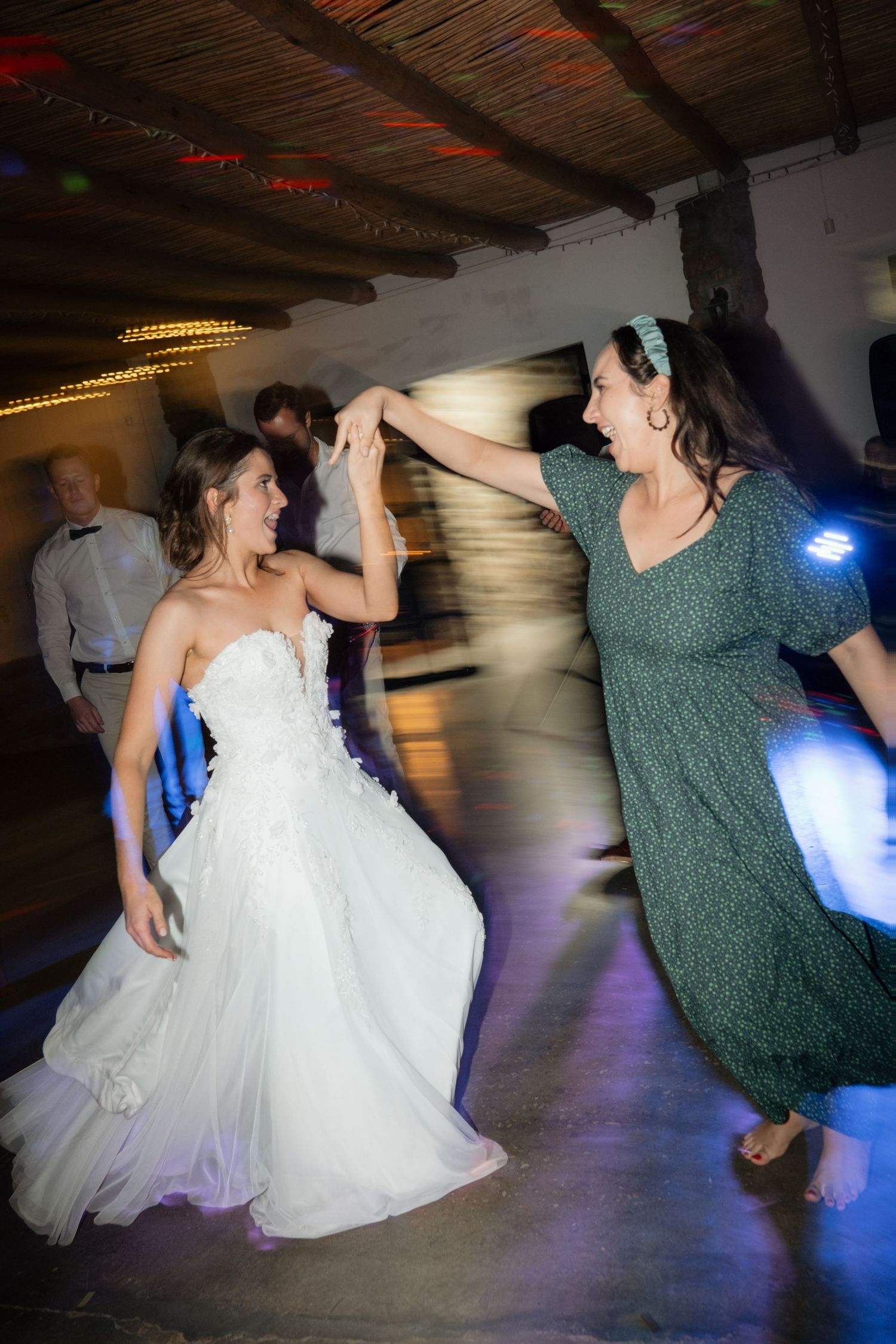 Bride in strapless white gown dancing energetically with female guest at wedding reception.