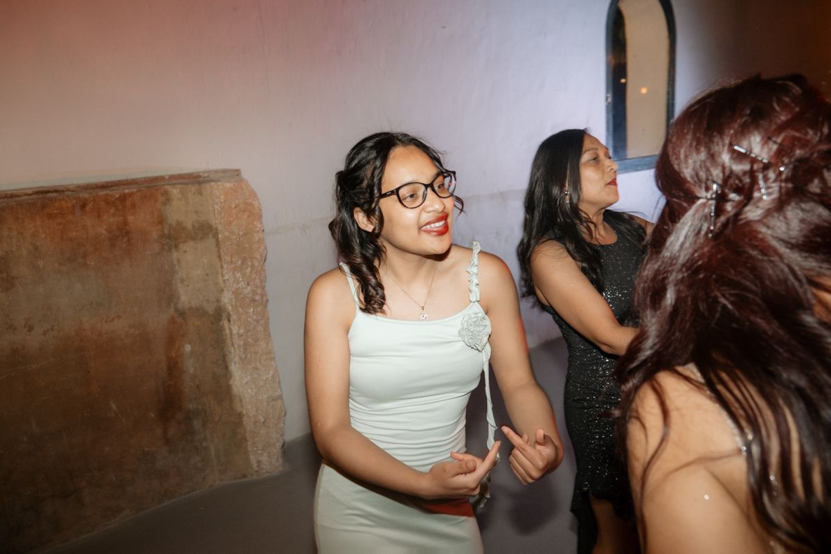 Young woman in white dress laughing with guests at an evening wedding reception party.