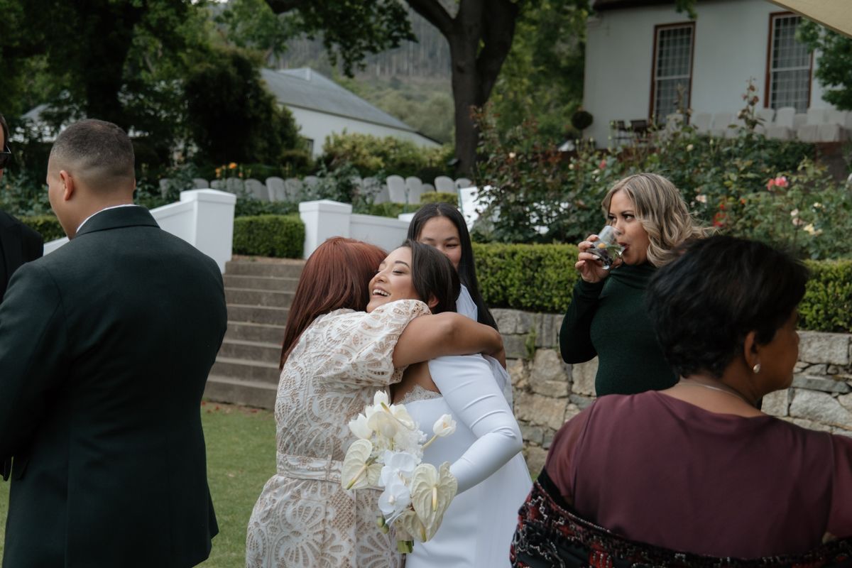 Wedding guests embracing and congratulating the bride in a white gown at an outdoor garden venue.