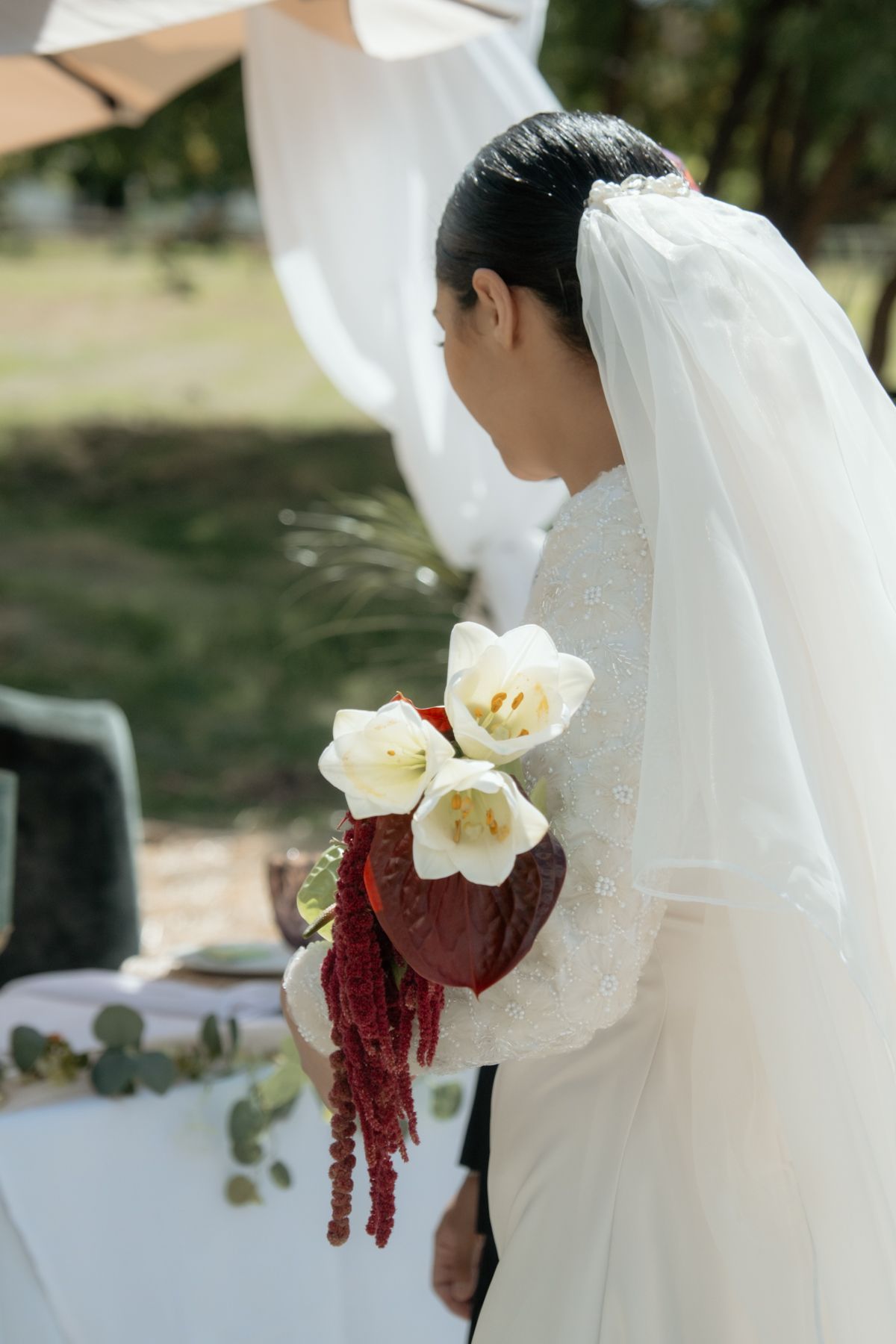 Bride holding a stunning bouquet of white tulips and deep red amaranthus at an outdoor wedding ceremony.