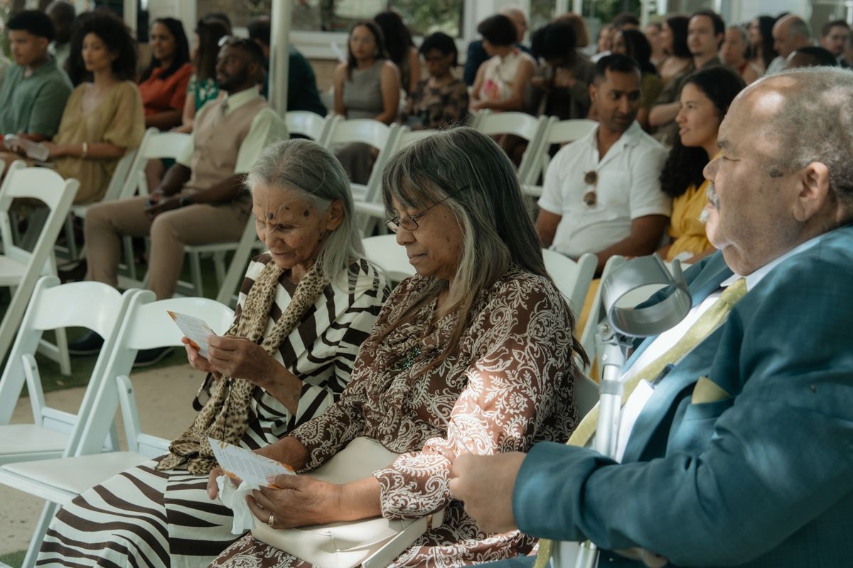 Diverse wedding guests seated in white chairs at an outdoor ceremony, dressed in elegant attire.