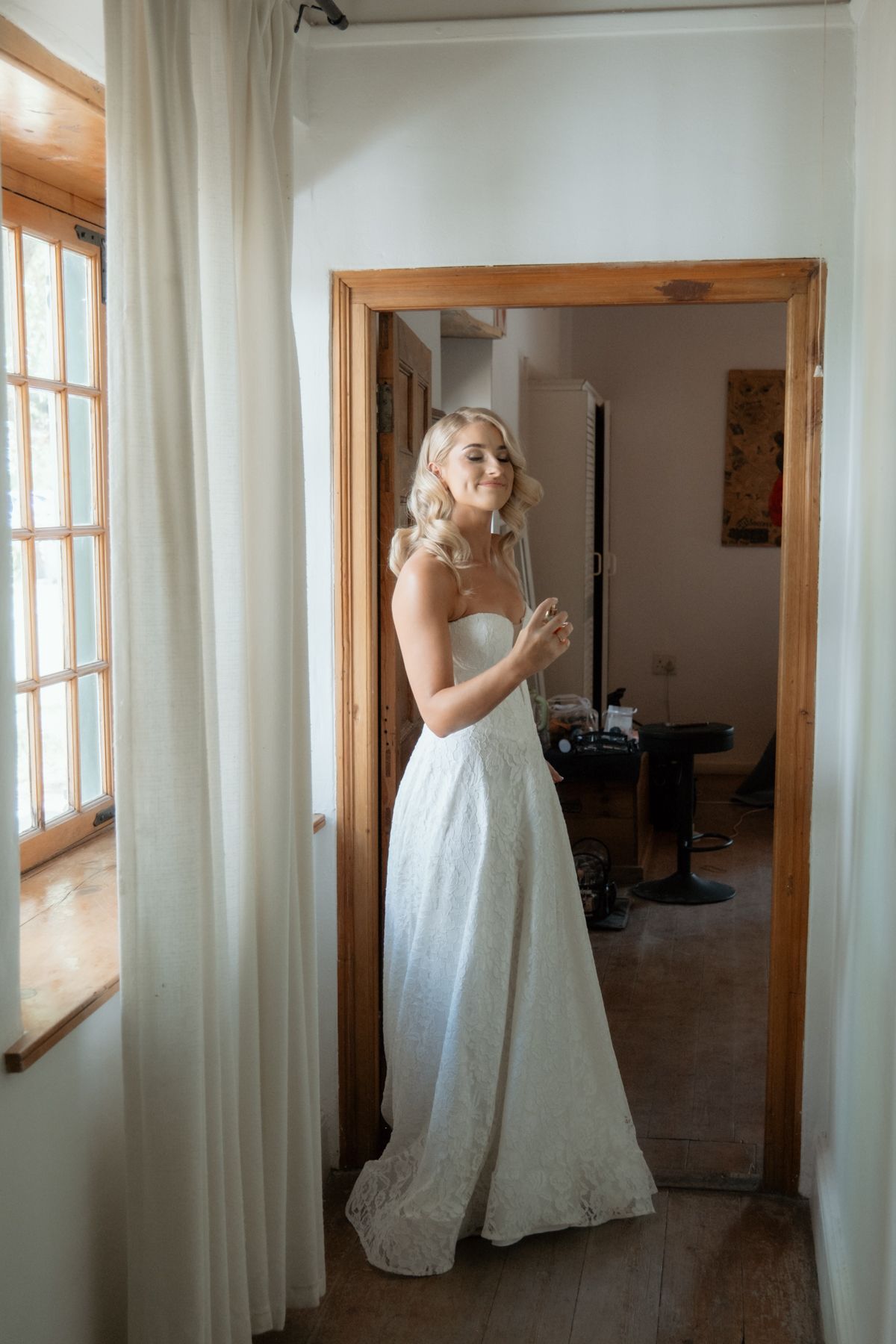 Elegant bride in a strapless lace wedding gown standing in a doorway on her wedding day.