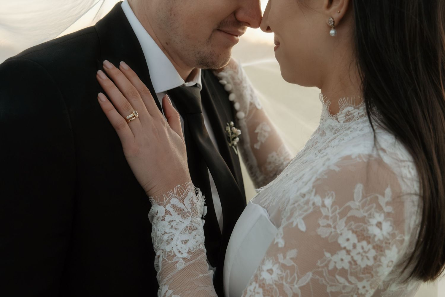 Bride and groom in elegant wedding attire share an intimate moment, nearly kissing.