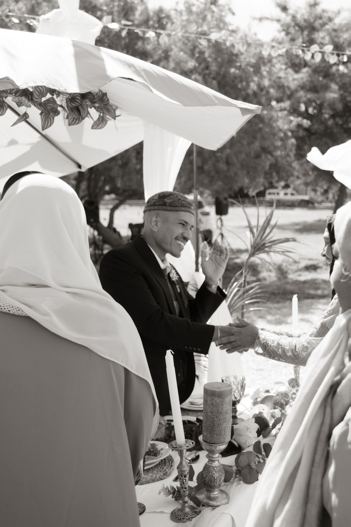 Black and white photo of a Jewish wedding ceremony under a chuppah with officiant and candles.