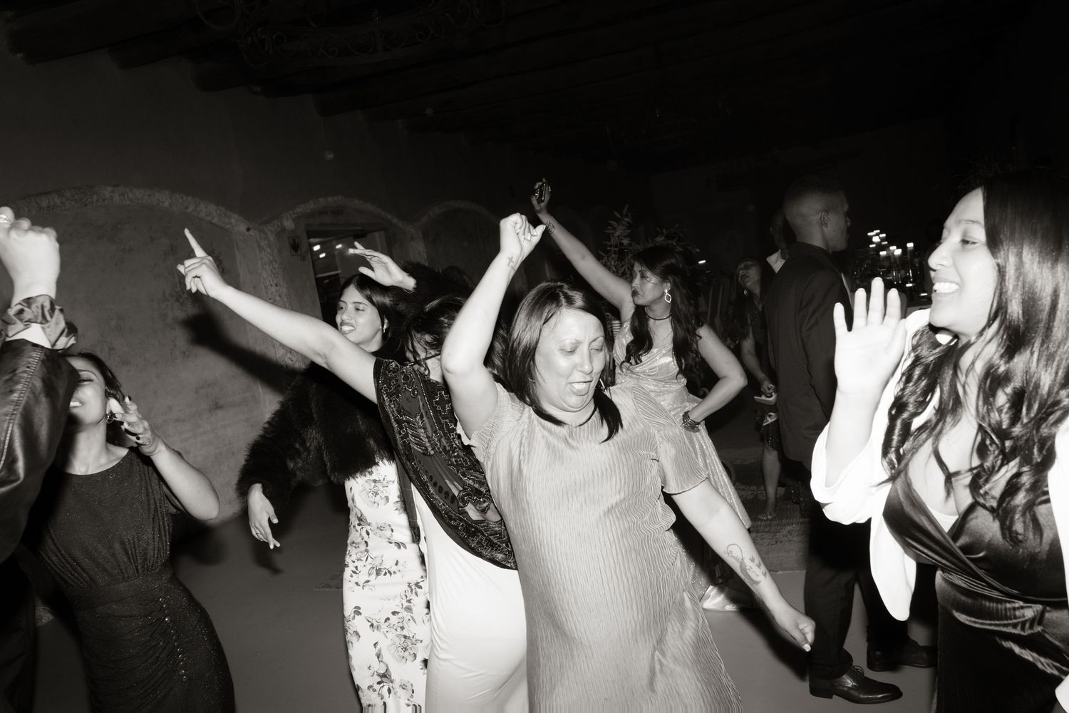 Wedding guests dancing energetically on the dance floor captured in black and white.