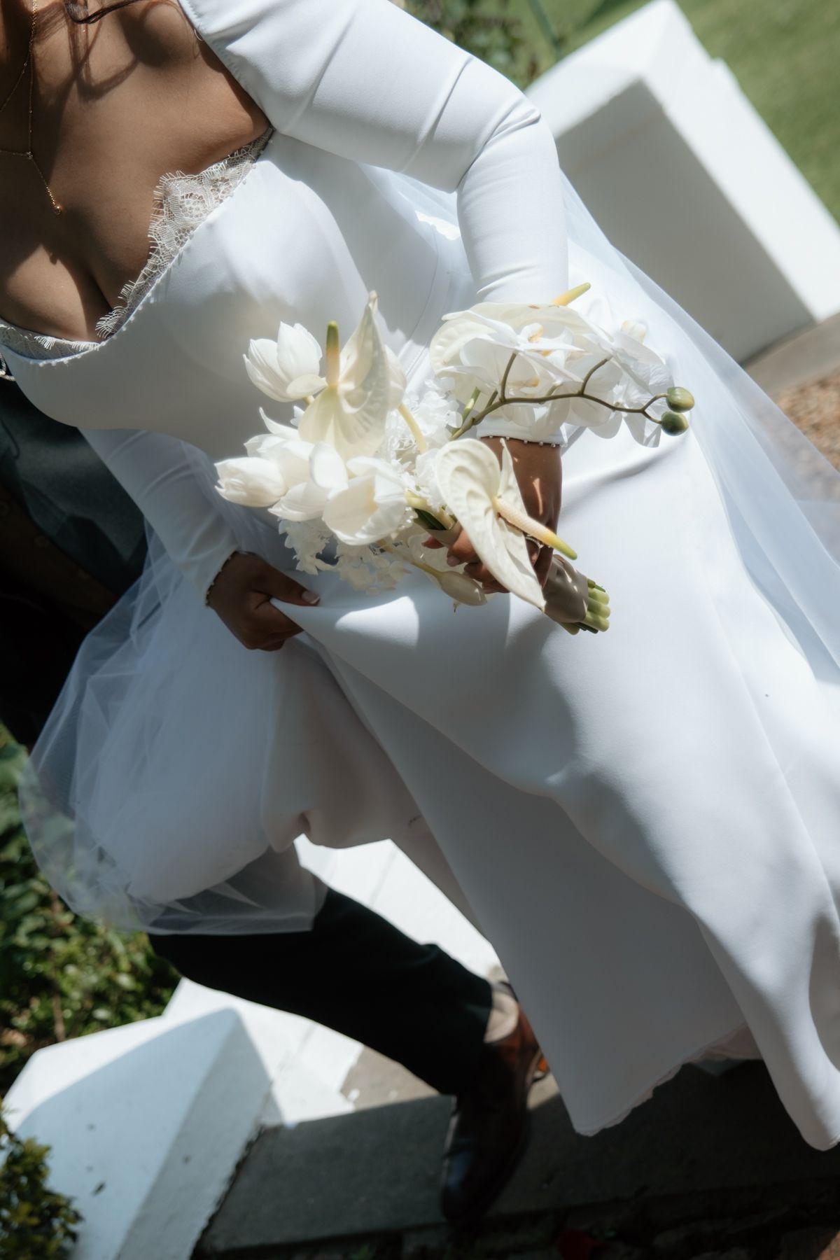 Close-up of bride in white long-sleeve wedding dress holding elegant white floral bouquet.