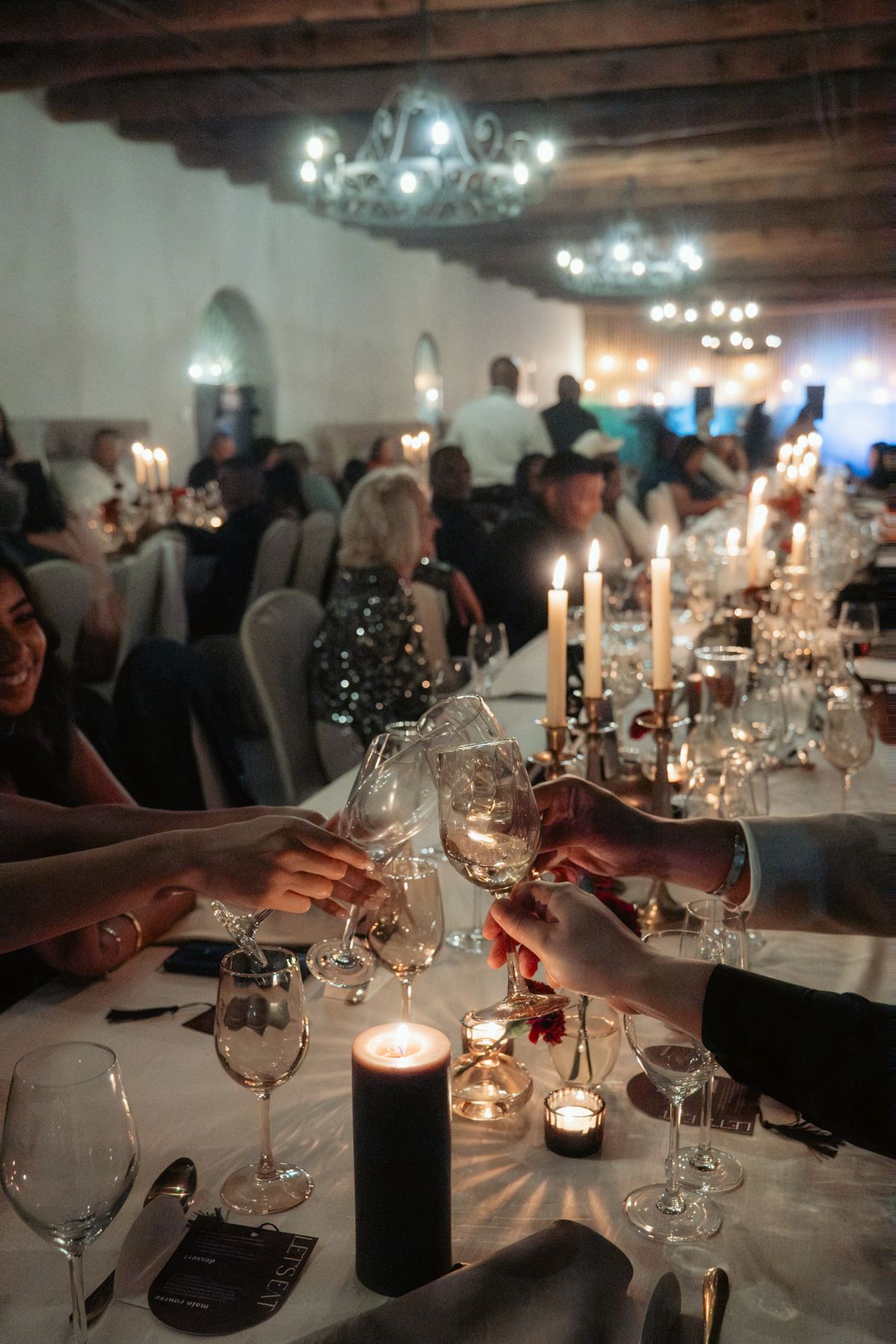 Wedding guests toasting with wine glasses by candlelight in a rustic reception venue.