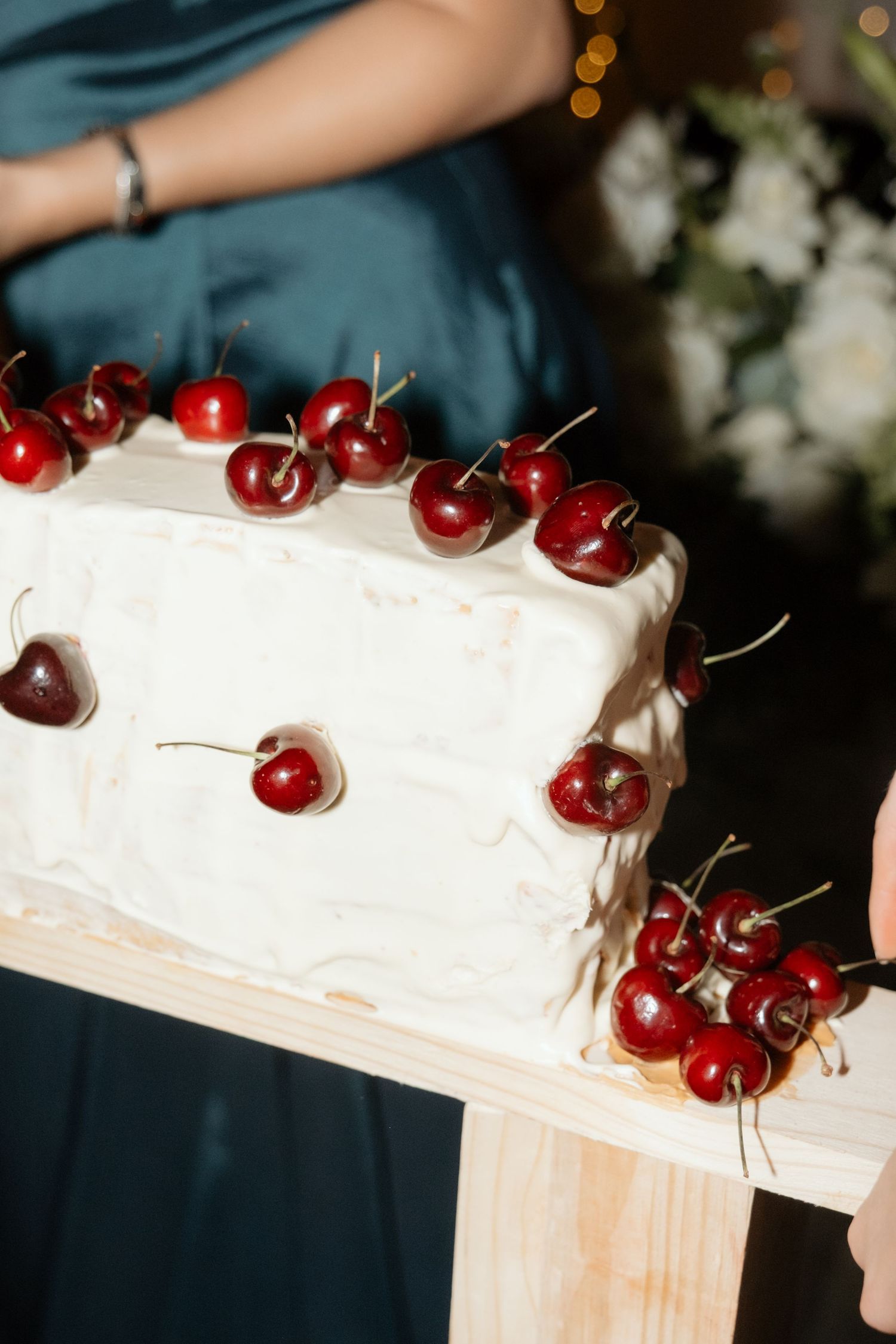 White wedding cake decorated with fresh red cherries on a rustic wooden stand.