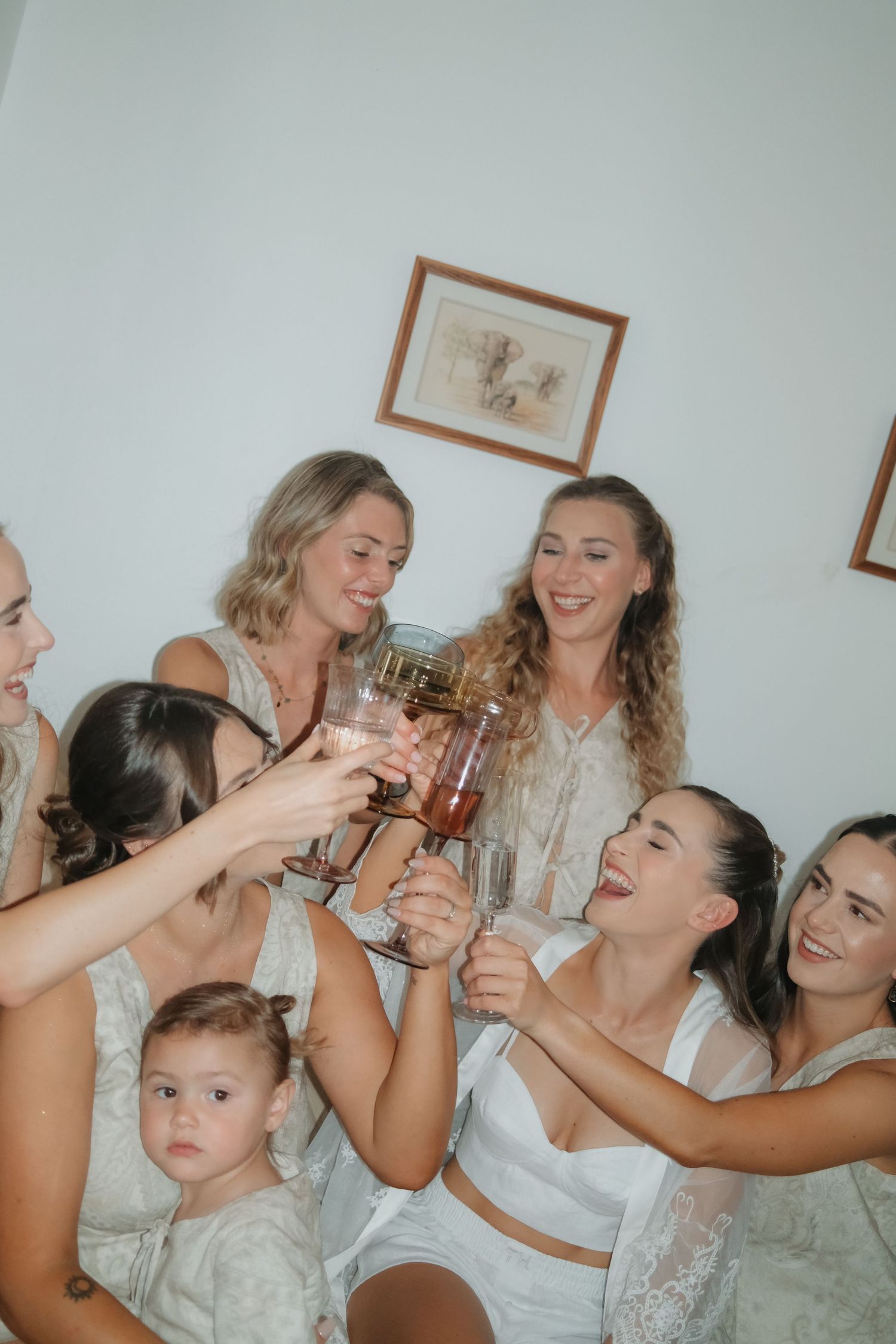 Bridesmaids in lace robes toasting with champagne glasses during wedding morning preparations.