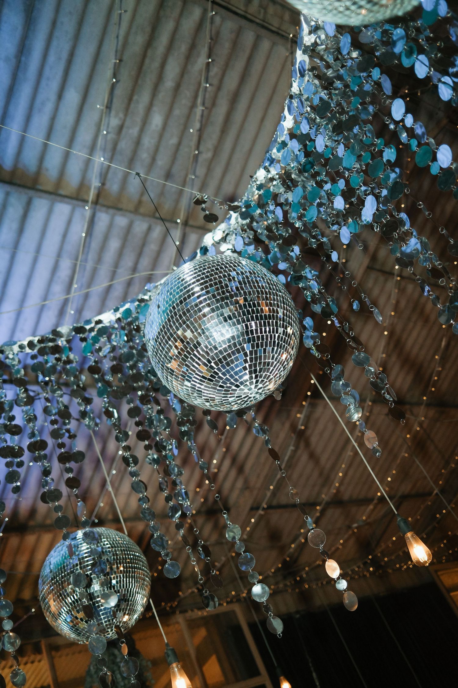 Sparkling disco balls hanging with sequin garlands in rustic wedding reception venue.