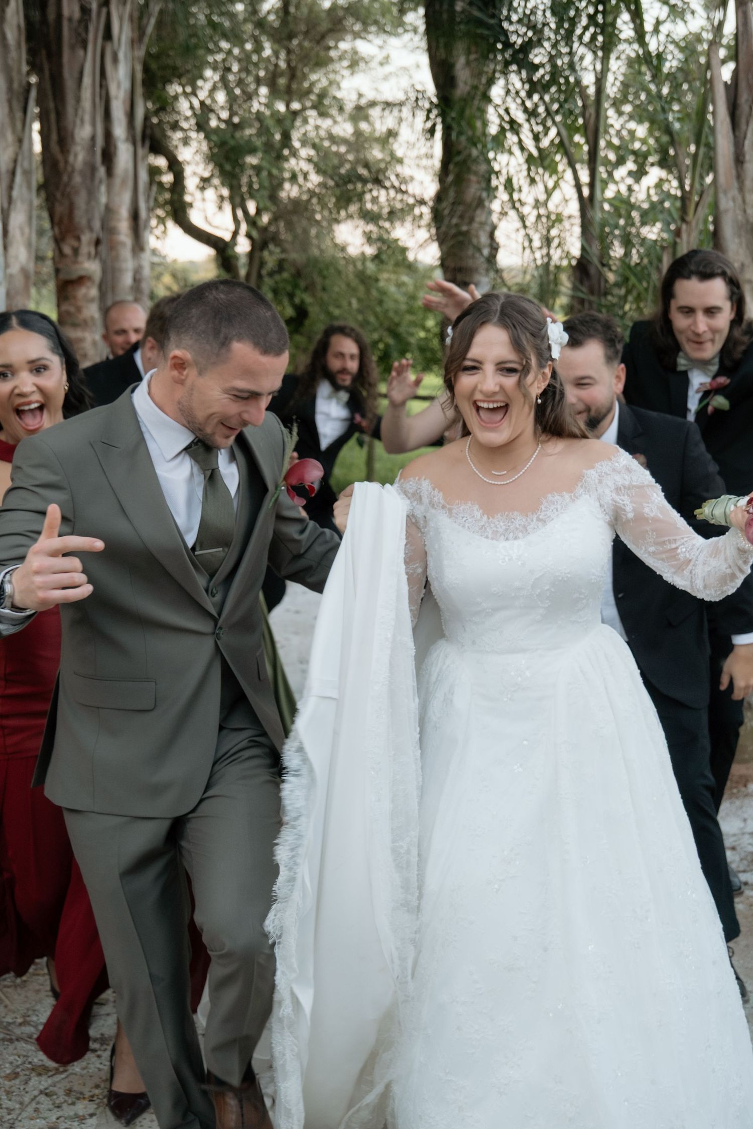 Joyful bride and groom walk together after ceremony surrounded by cheering wedding guests outdoors.