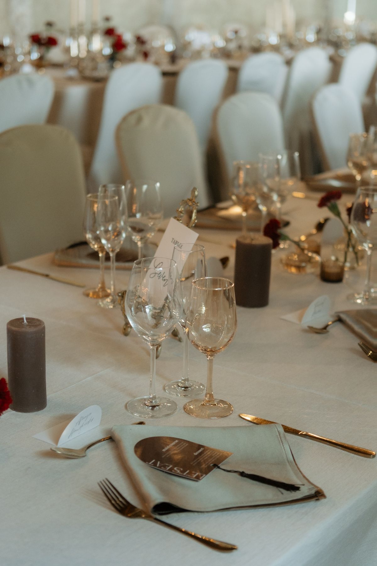 Elegant wedding reception table set with crystal wine glasses, gold cutlery, grey candles, and white linen tablecloth.