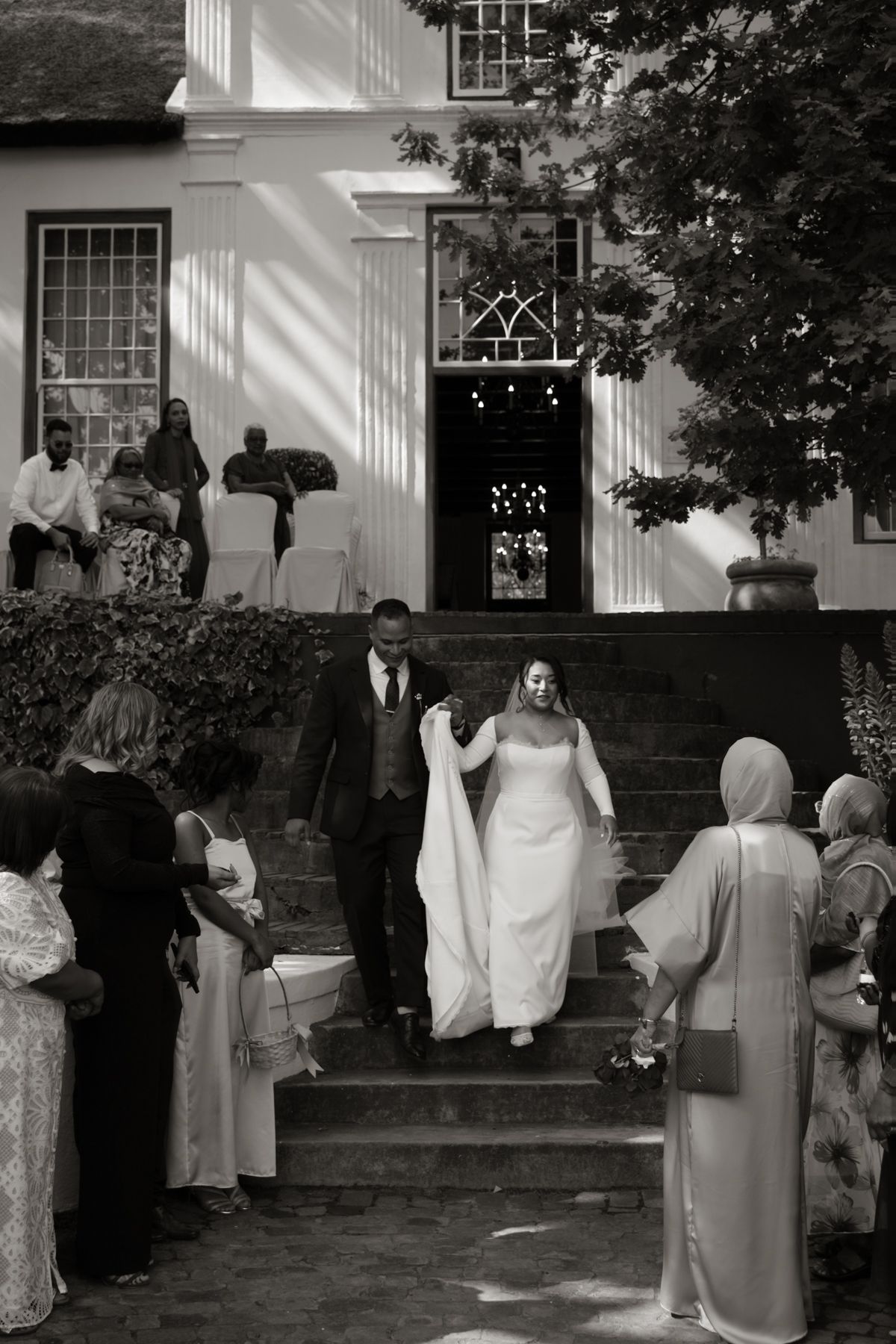 Black and white photo of bride and groom descending stone steps after outdoor wedding ceremony.