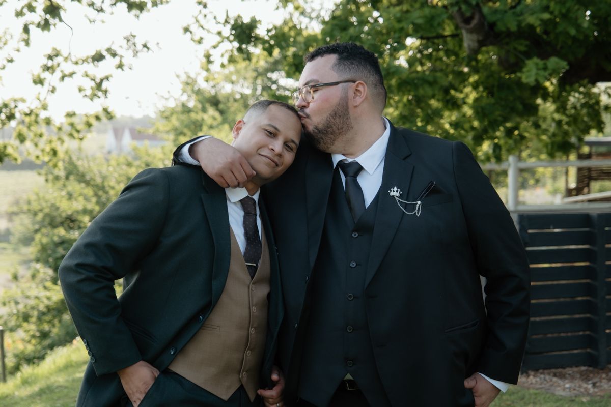 Two groomsmen share a playful moment together outdoors under a tree at a wedding.