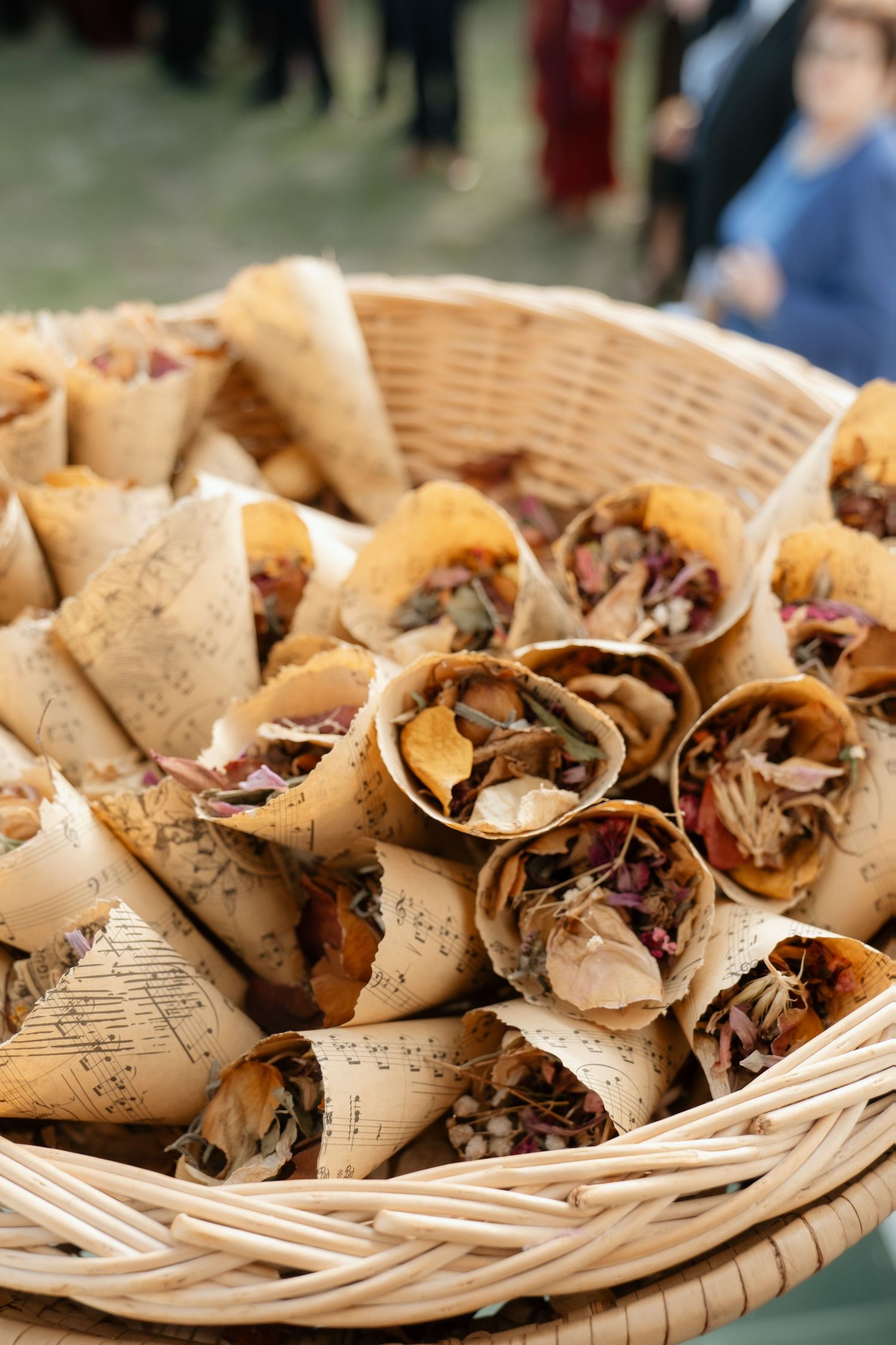Close-up of handmade paper cones filled with dried rose petals in a woven wicker basket at a wedding.