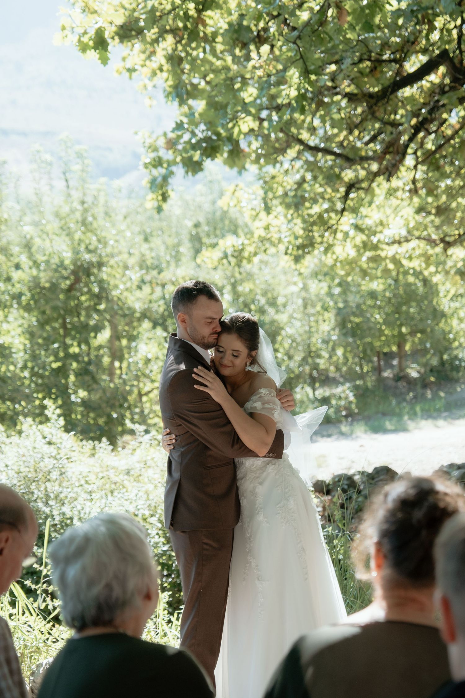Bride and groom sharing a tender embrace during their outdoor wedding ceremony under a large tree.