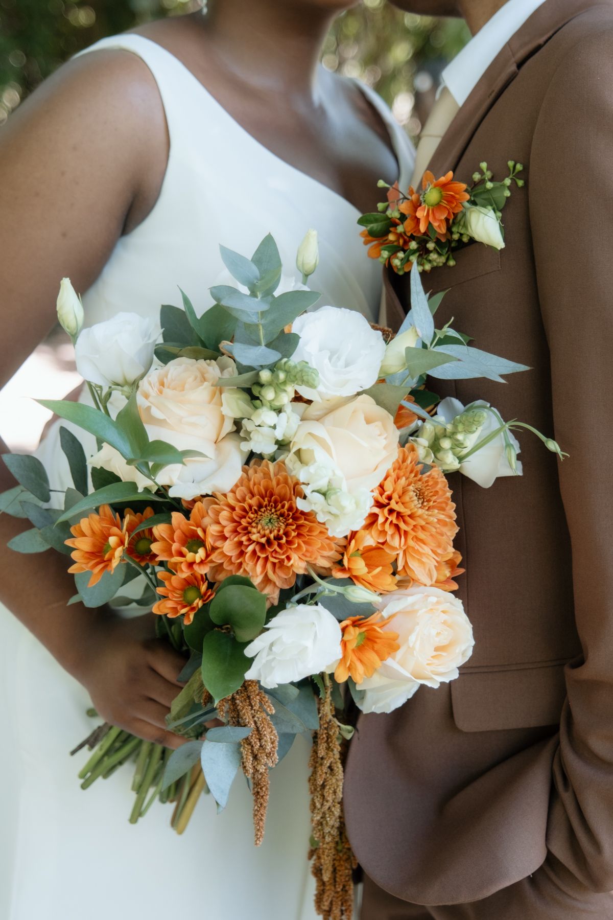 Close-up of bridal bouquet featuring orange dahlias, white roses, and eucalyptus with matching groom boutonniere.