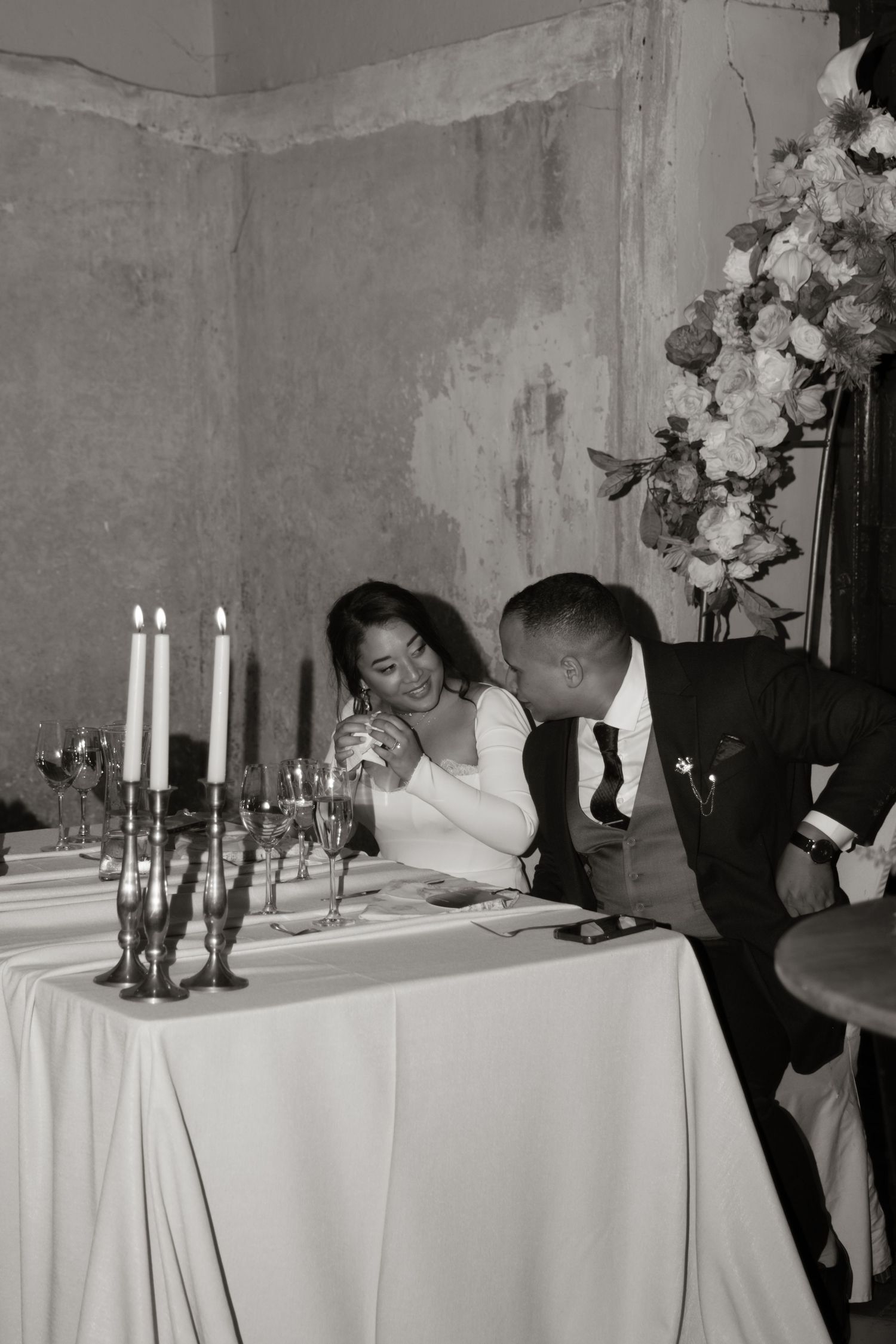 Black and white photo of a bride and groom sharing an intimate moment at their wedding reception table with candles.