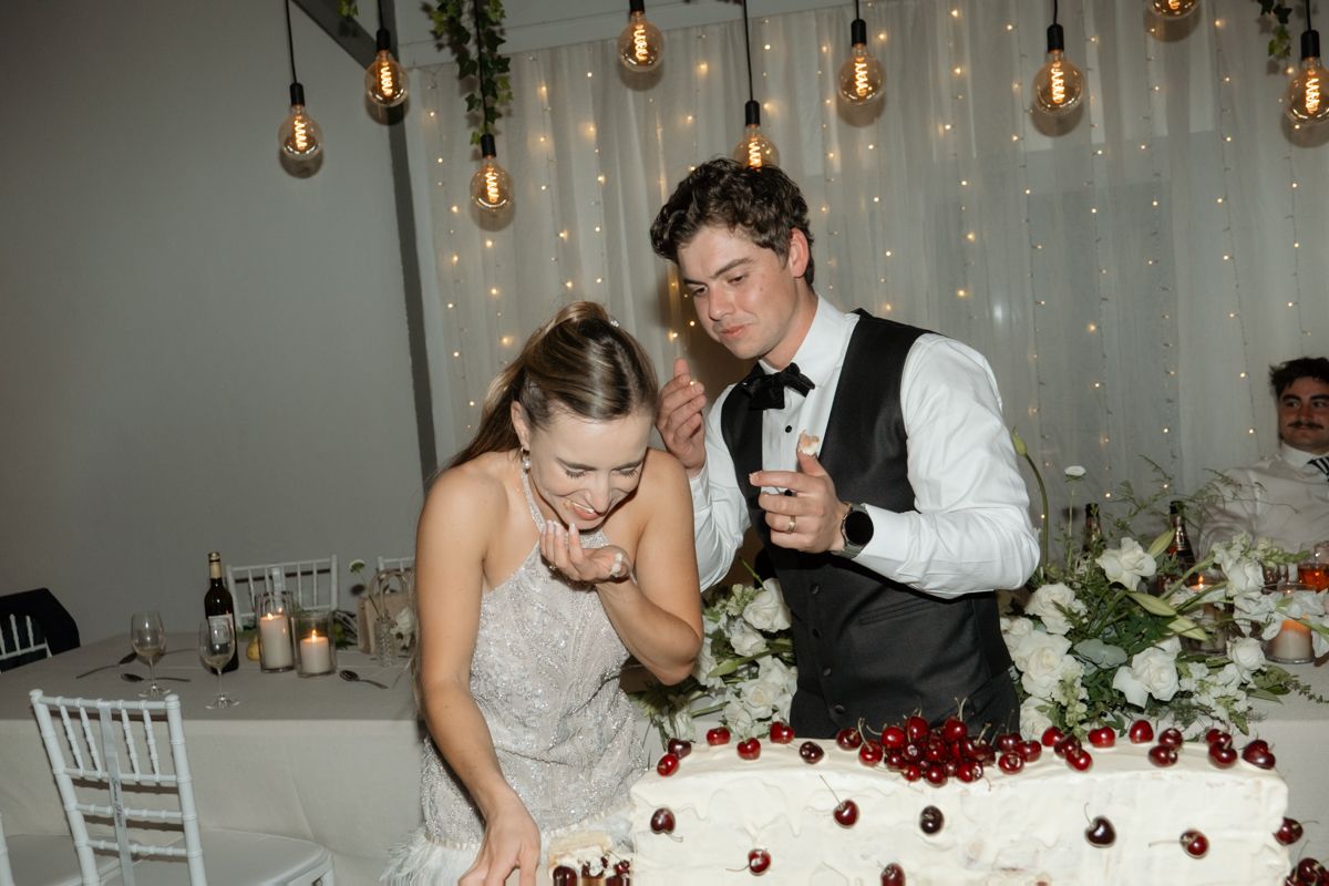 Bride and groom cut white wedding cake decorated with fresh cherries at romantic reception.