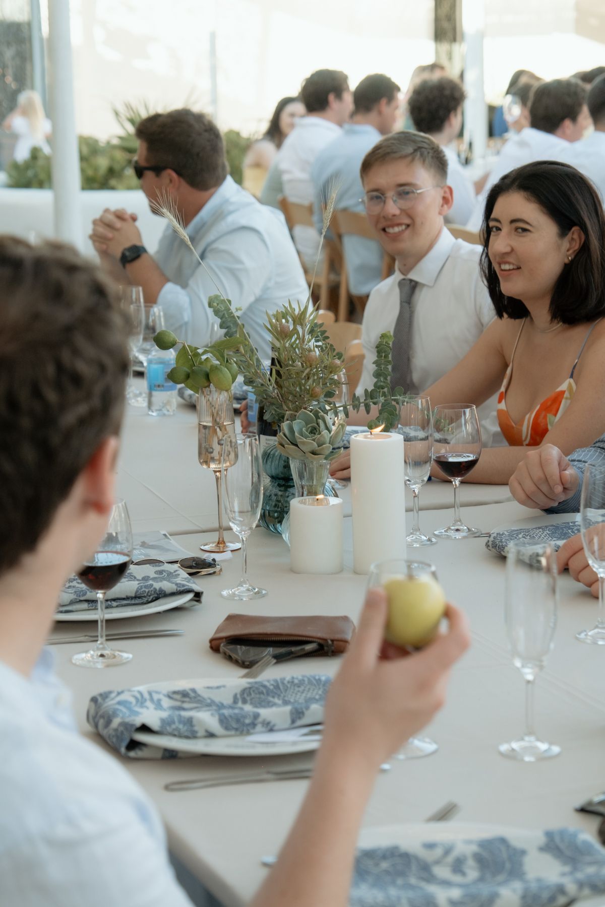 Wedding guests in formal attire enjoying dinner conversation at elegantly decorated reception table with candles and florals.