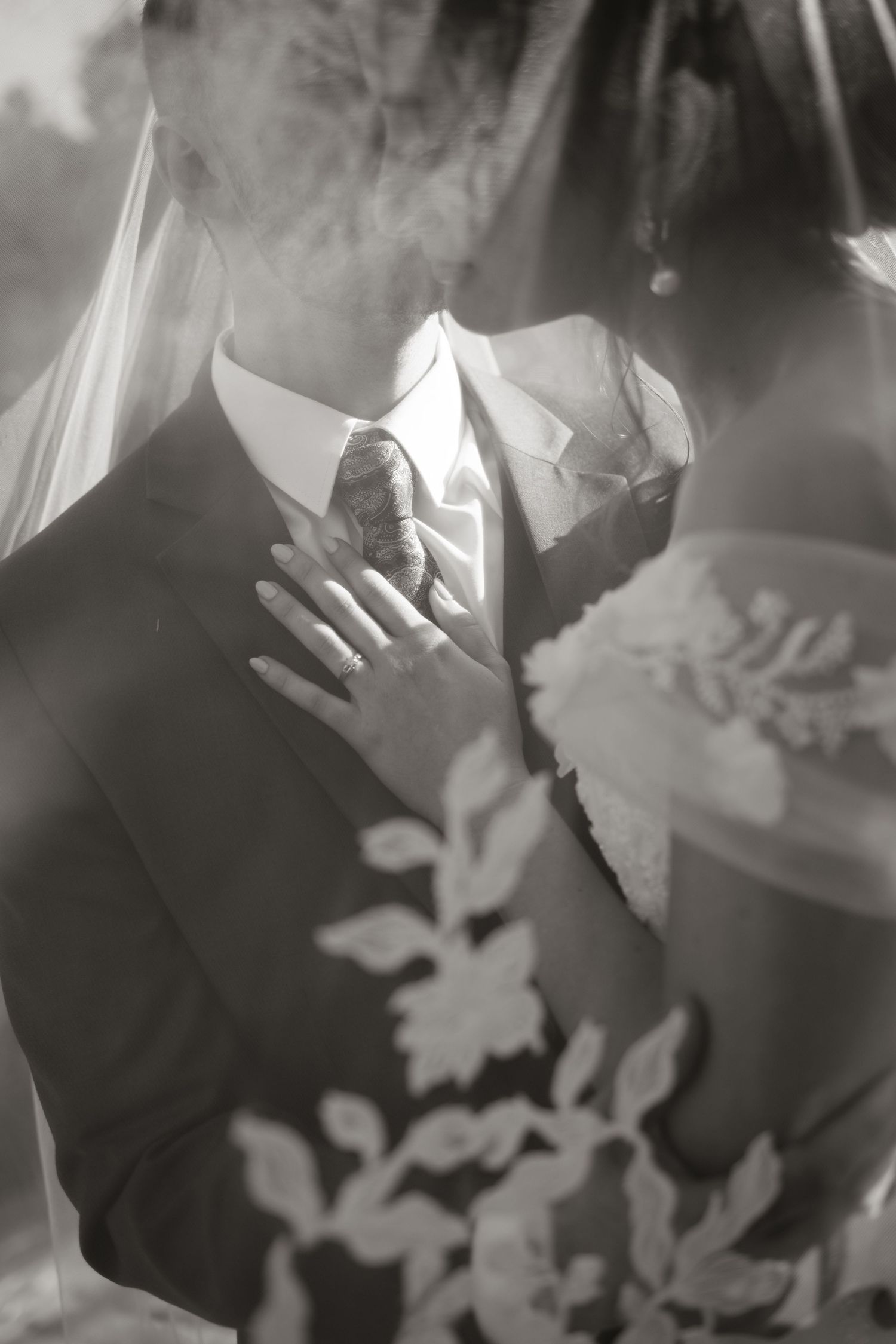 Black and white intimate photo of bride and groom kissing under veil showing wedding ring.