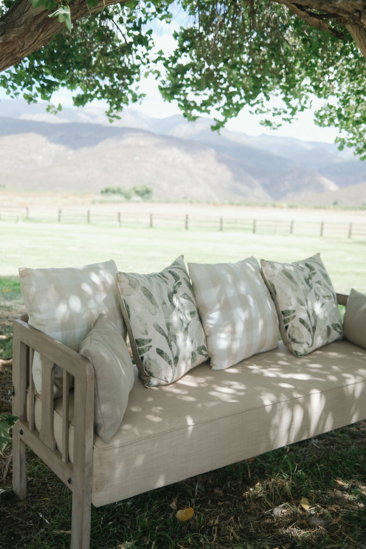 Elegant outdoor wedding lounge seating with neutral cushions and botanical pillows set against a scenic mountain backdrop.